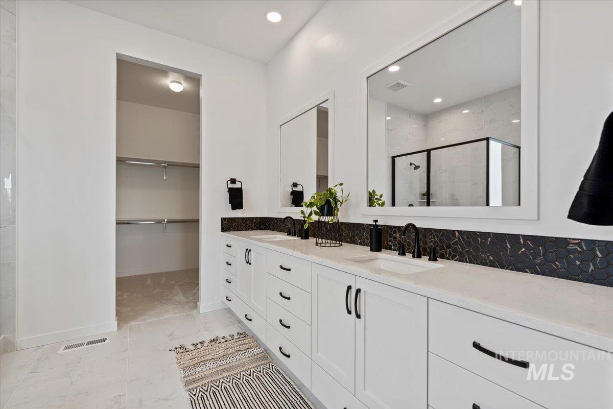 Bathroom with a marble finish shower, double vanity, a spacious closet, and recessed lighting