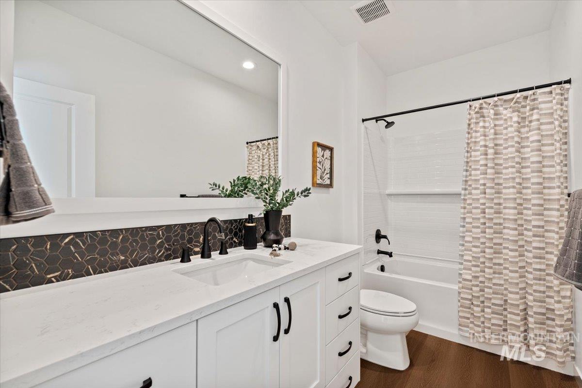 Full bathroom featuring vanity, dark wood-type flooring, shower / bath combo with shower curtain, recessed lighting, and tasteful backsplash