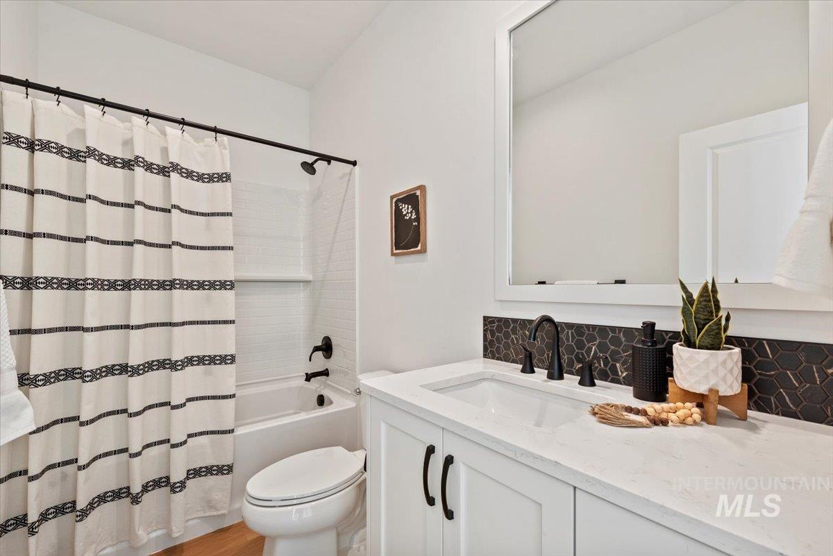 Full bathroom featuring vanity, decorative backsplash, shower / tub combo, and light wood-style flooring