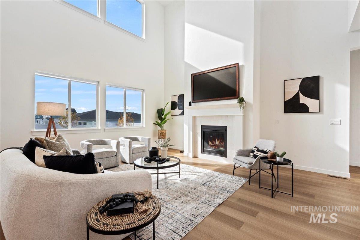 Living room with a towering ceiling, plenty of natural light, light wood-style flooring, and a glass covered fireplace