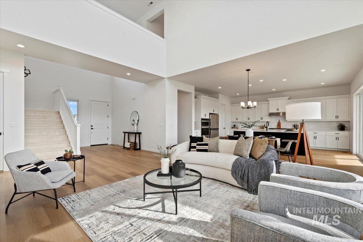 Living room featuring stairway, light wood-type flooring, recessed lighting, a chandelier, and a high ceiling