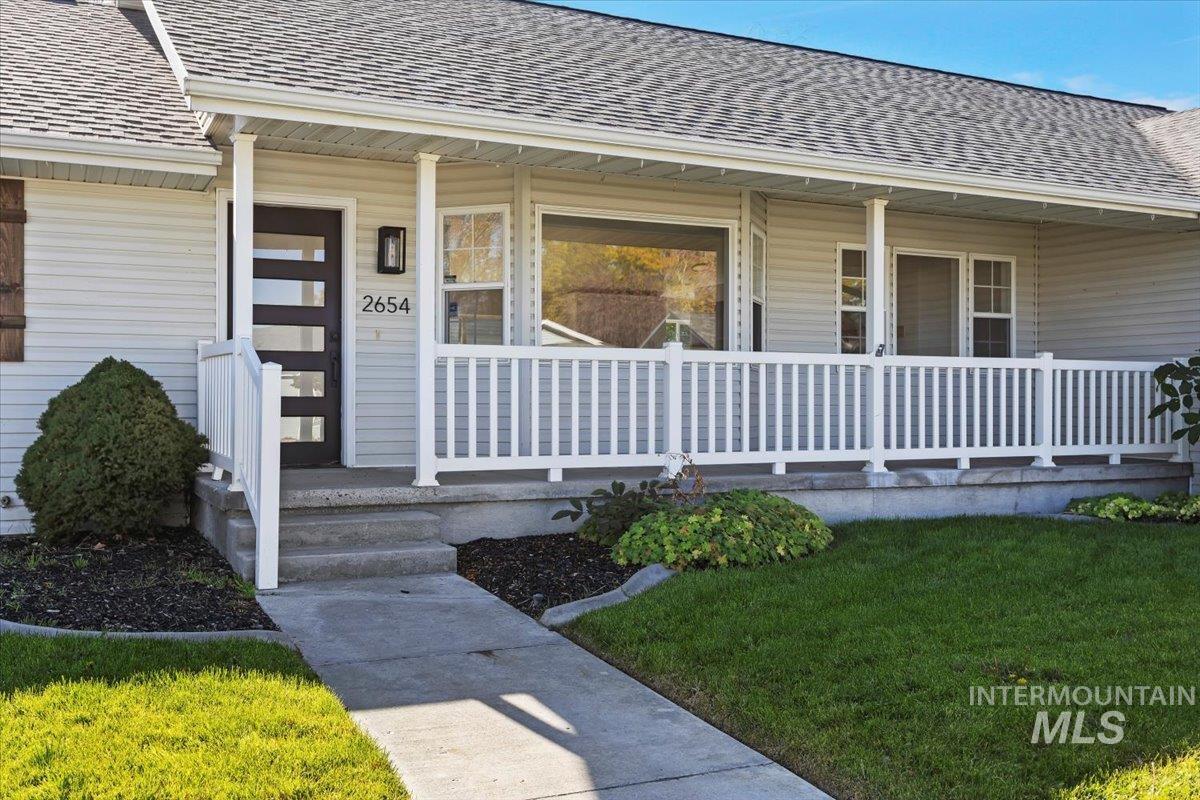 Property entrance with roof with shingles, covered porch, and a yard