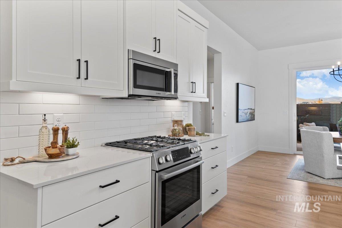 Kitchen featuring appliances with stainless steel finishes, white cabinetry, light wood-style floors, tasteful backsplash, and light stone counters