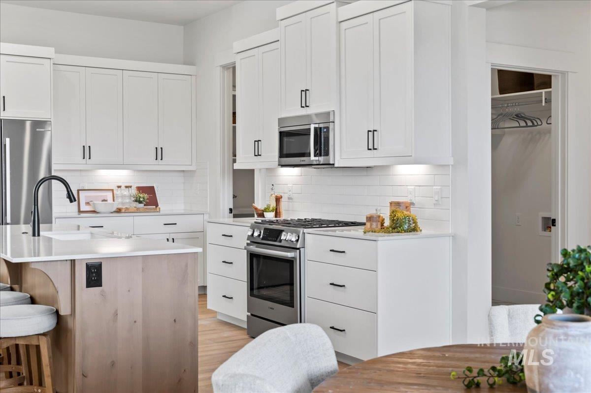 Kitchen featuring appliances with stainless steel finishes, a kitchen bar, white cabinetry, and tasteful backsplash