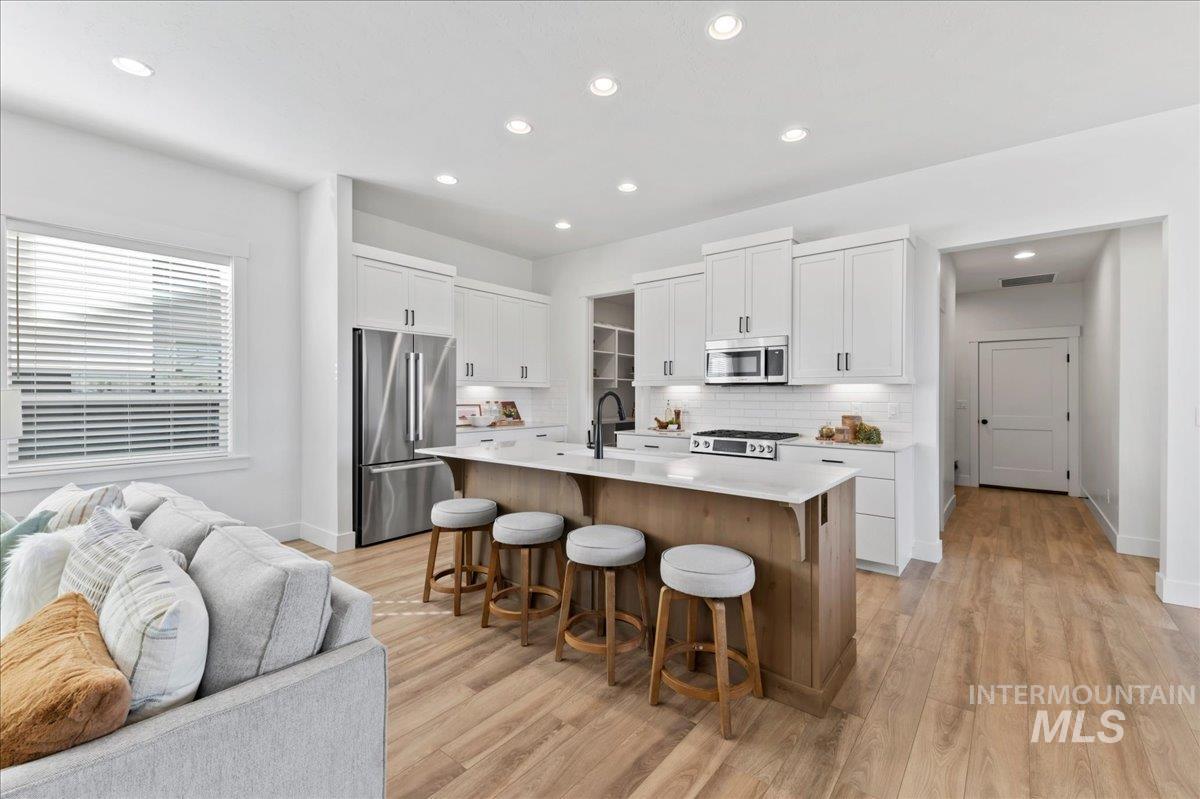 Kitchen with decorative backsplash, white cabinets, stainless steel appliances, an island with sink, and recessed lighting