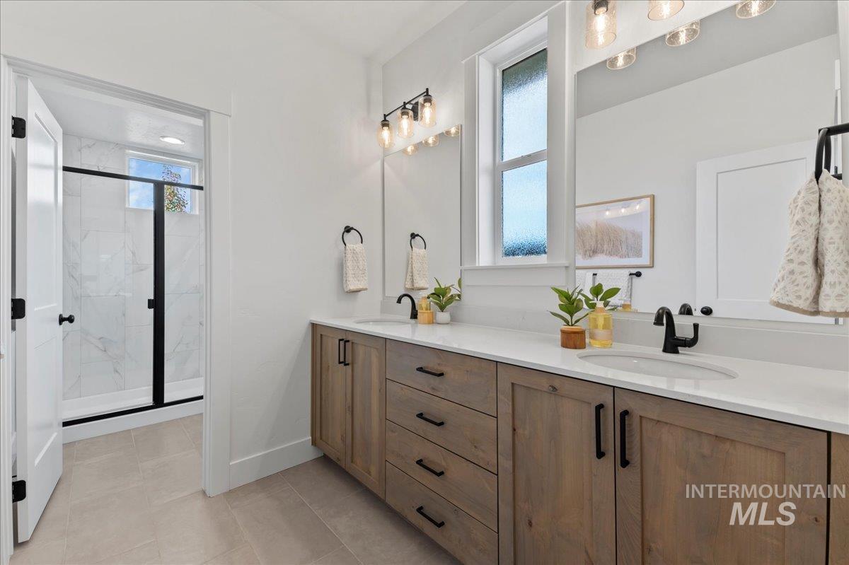 Full bathroom with double vanity, a marble finish shower, and light tile patterned floors