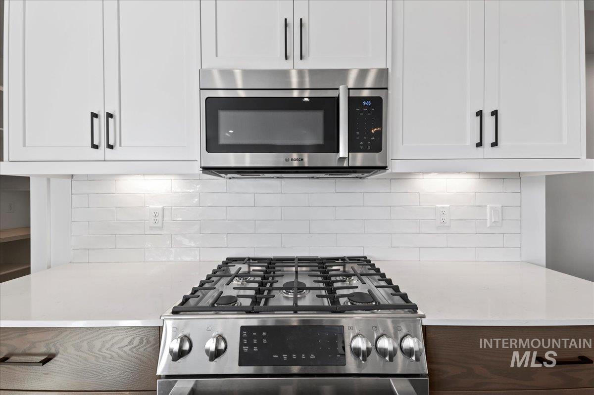 Kitchen with backsplash, appliances with stainless steel finishes, light stone counters, and white cabinets
