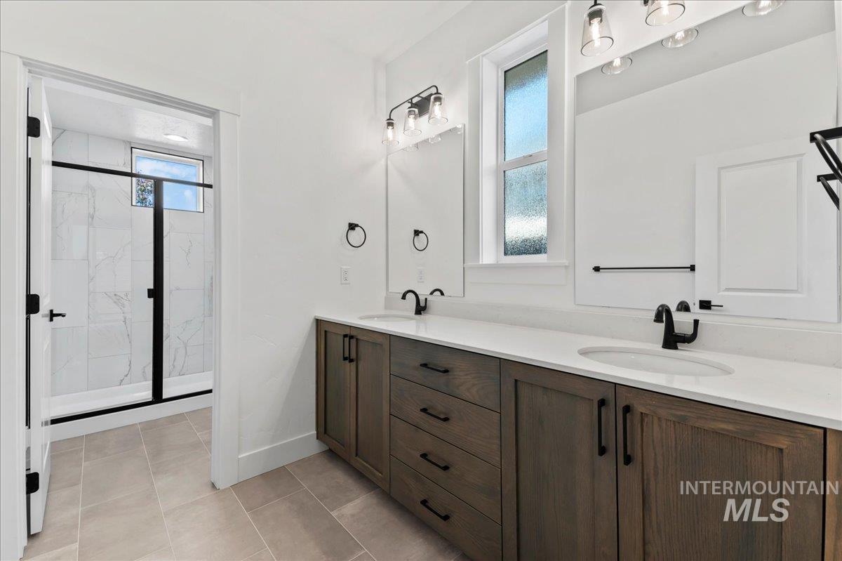 Bathroom with double vanity, a marble finish shower, and light tile patterned flooring