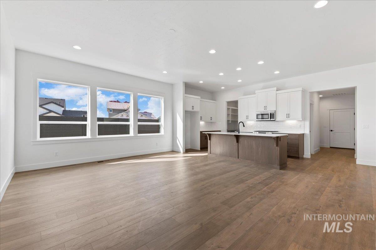 Kitchen with white cabinets, open floor plan, a breakfast bar, a center island with sink, and light countertops
