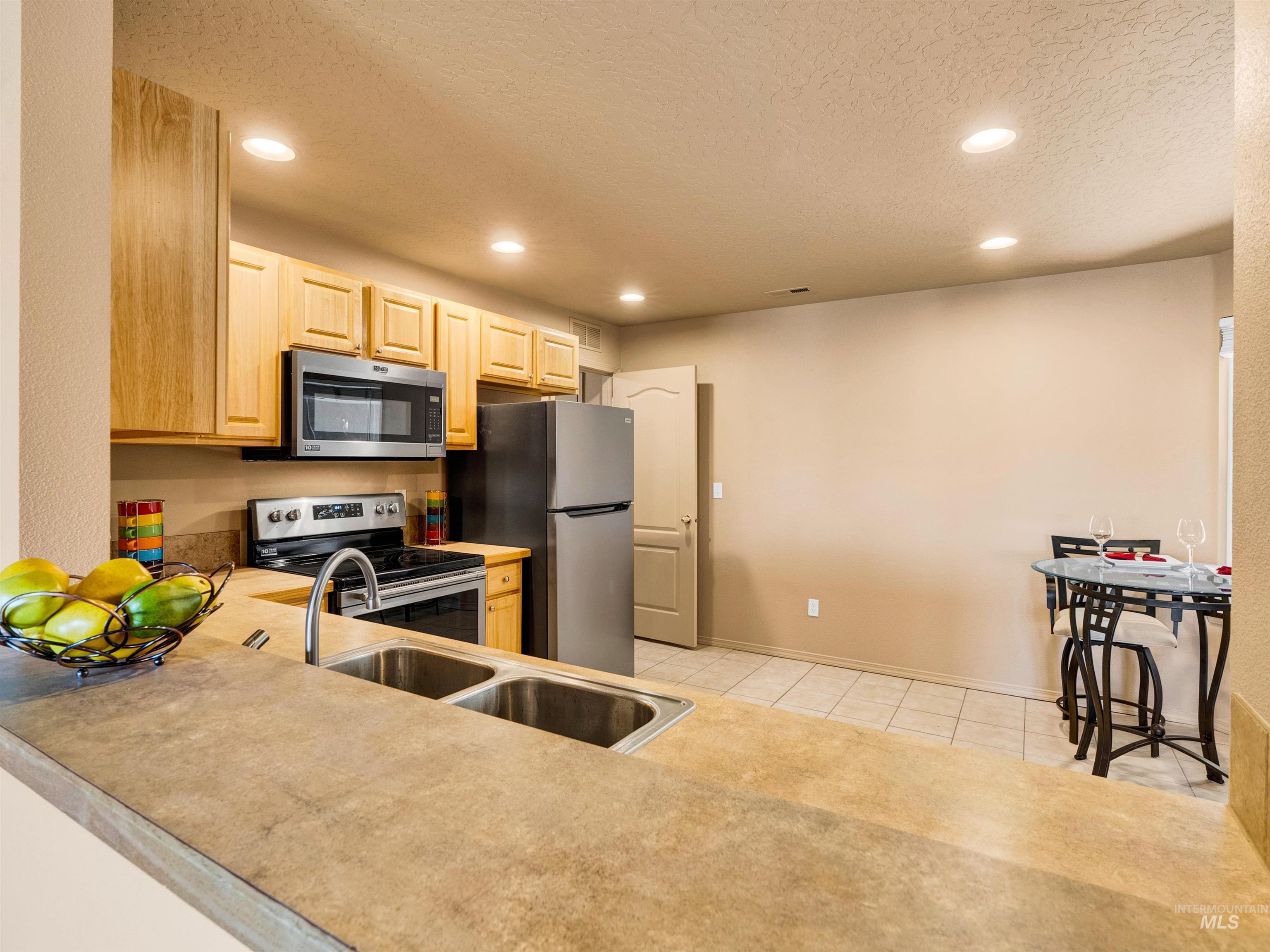 Kitchen with stainless steel appliances, light brown cabinetry, a textured ceiling, light countertops, and light tile patterned floors