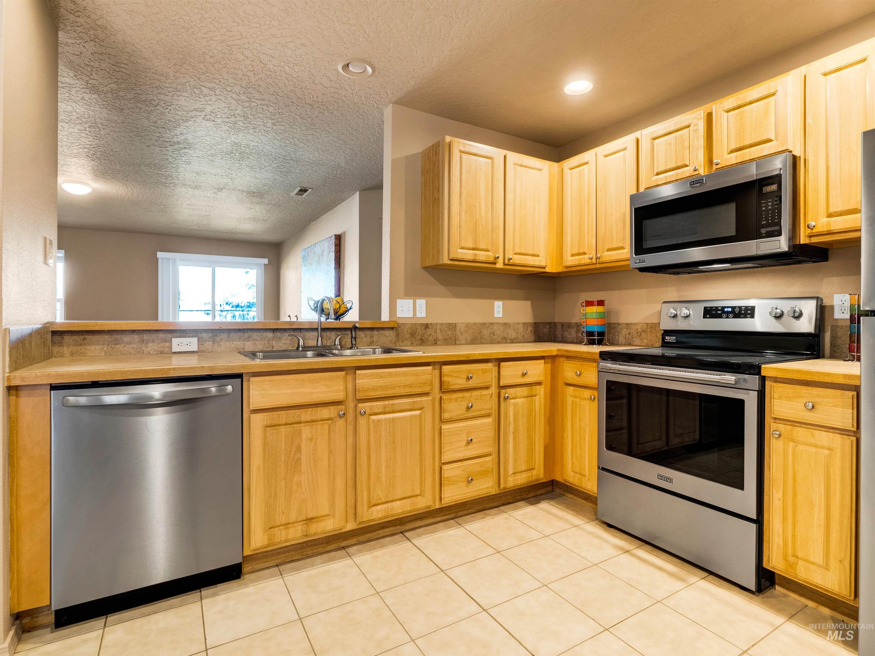Kitchen with appliances with stainless steel finishes, a textured ceiling, light tile patterned flooring, recessed lighting, and light brown cabinets