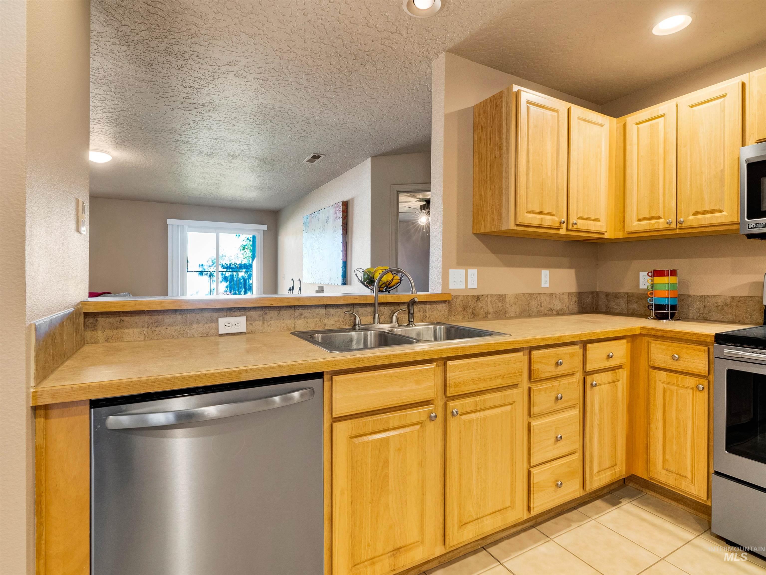 Kitchen with appliances with stainless steel finishes, light countertops, light tile patterned floors, a textured ceiling, and light brown cabinets