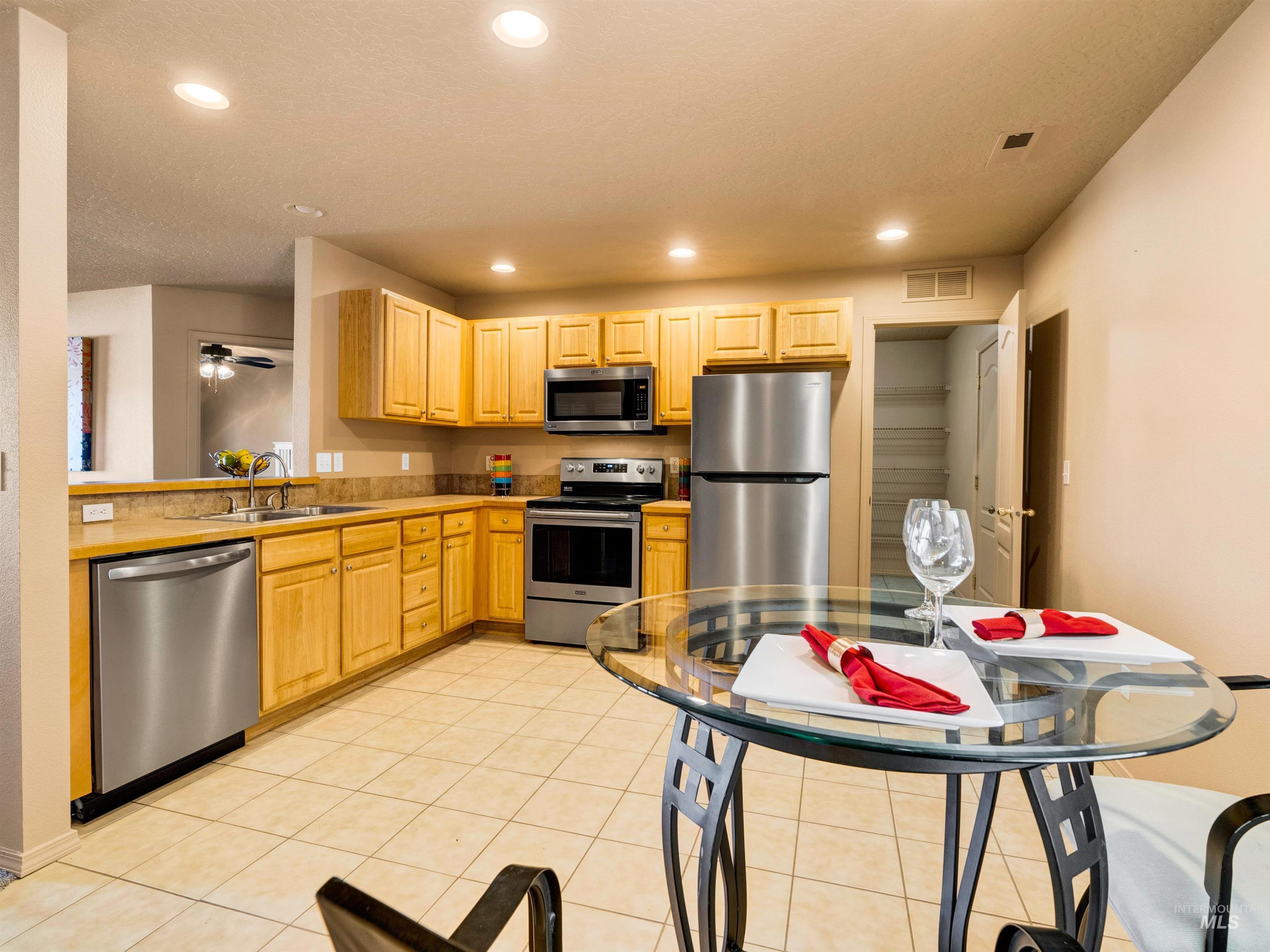 Kitchen with appliances with stainless steel finishes, light brown cabinetry, recessed lighting, light tile patterned floors, and ceiling fan