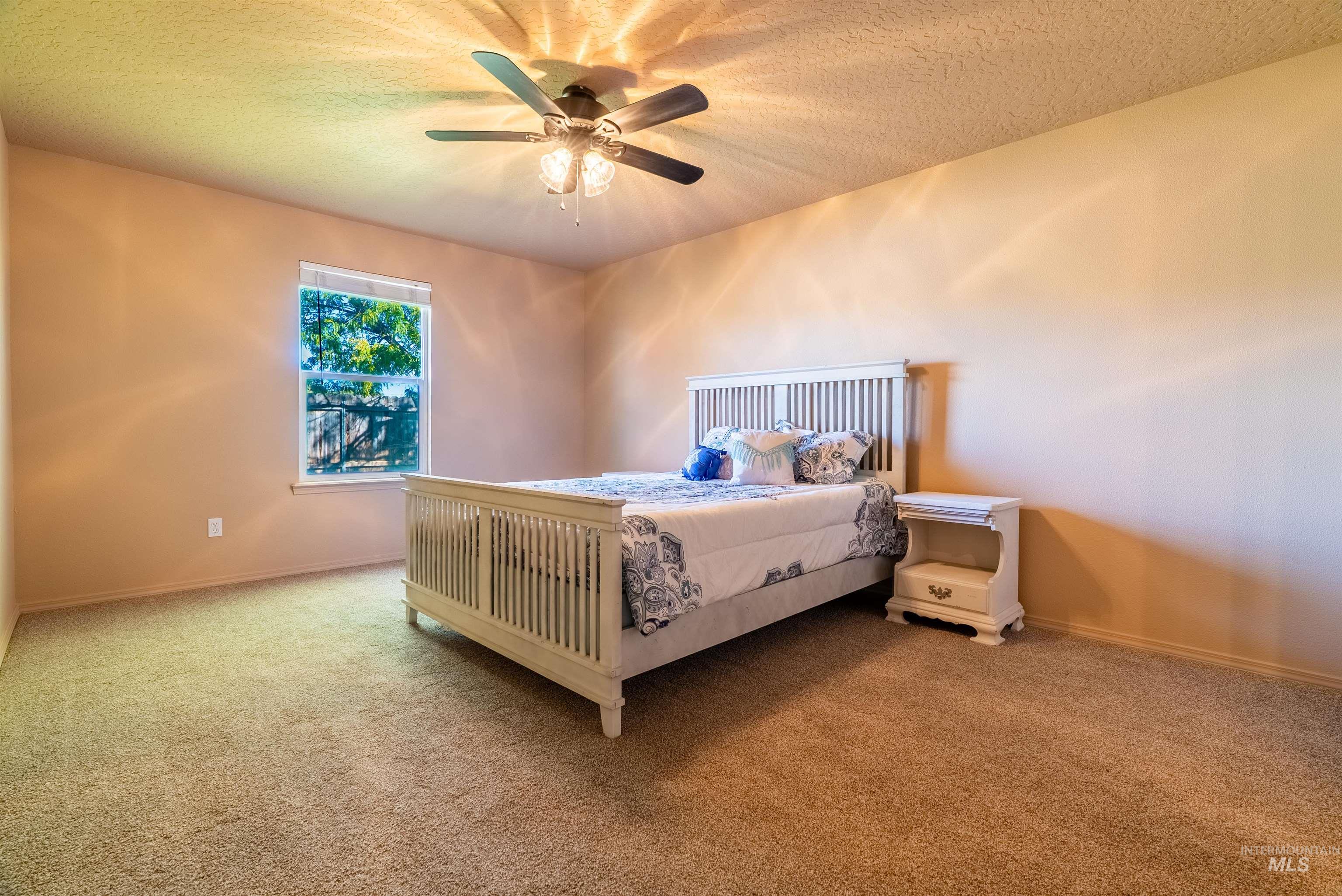 Carpeted bedroom with a textured ceiling and ceiling fan