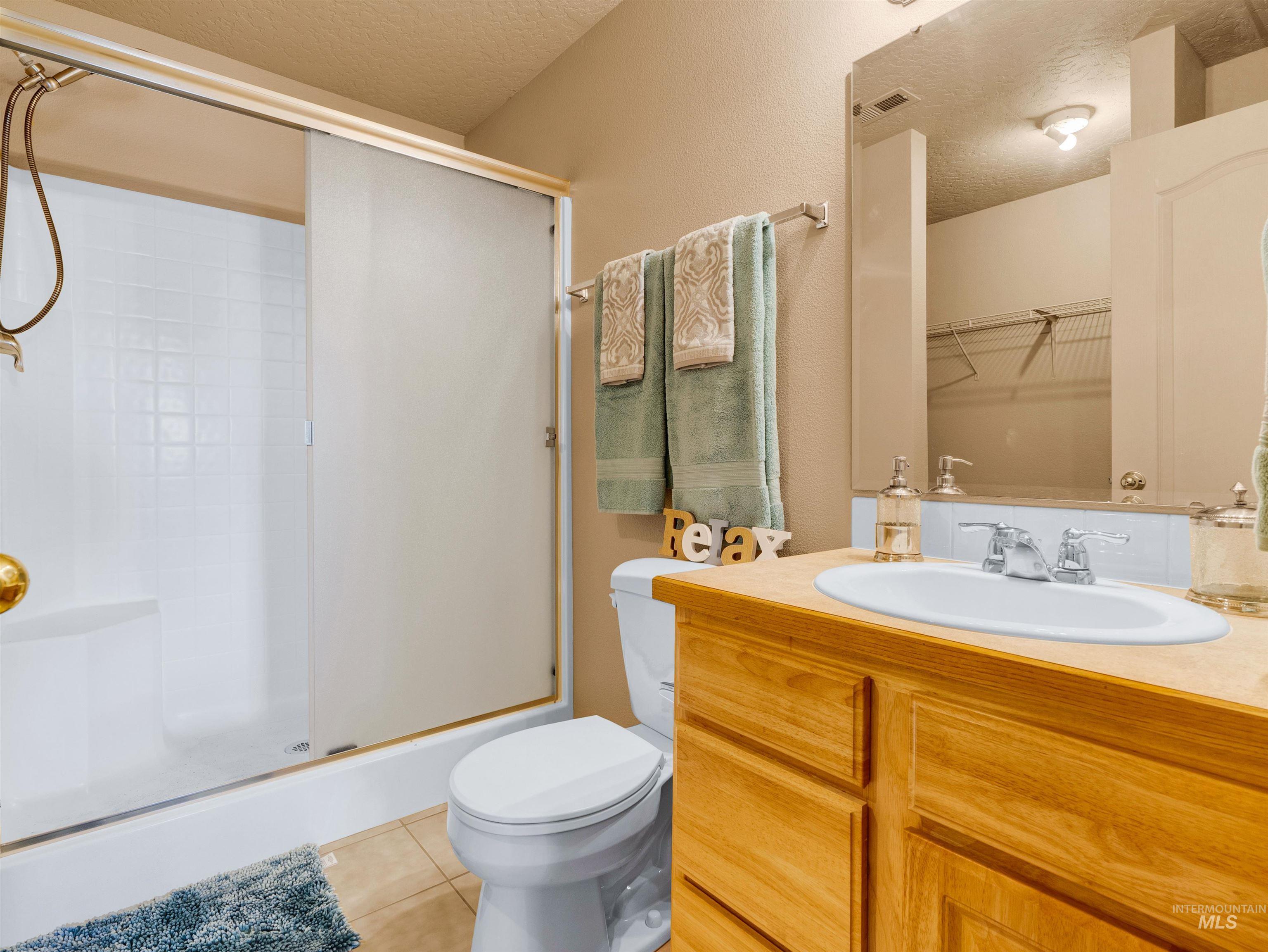Full bathroom with light tile patterned flooring, a textured ceiling, vanity, a shower stall, and a walk in closet