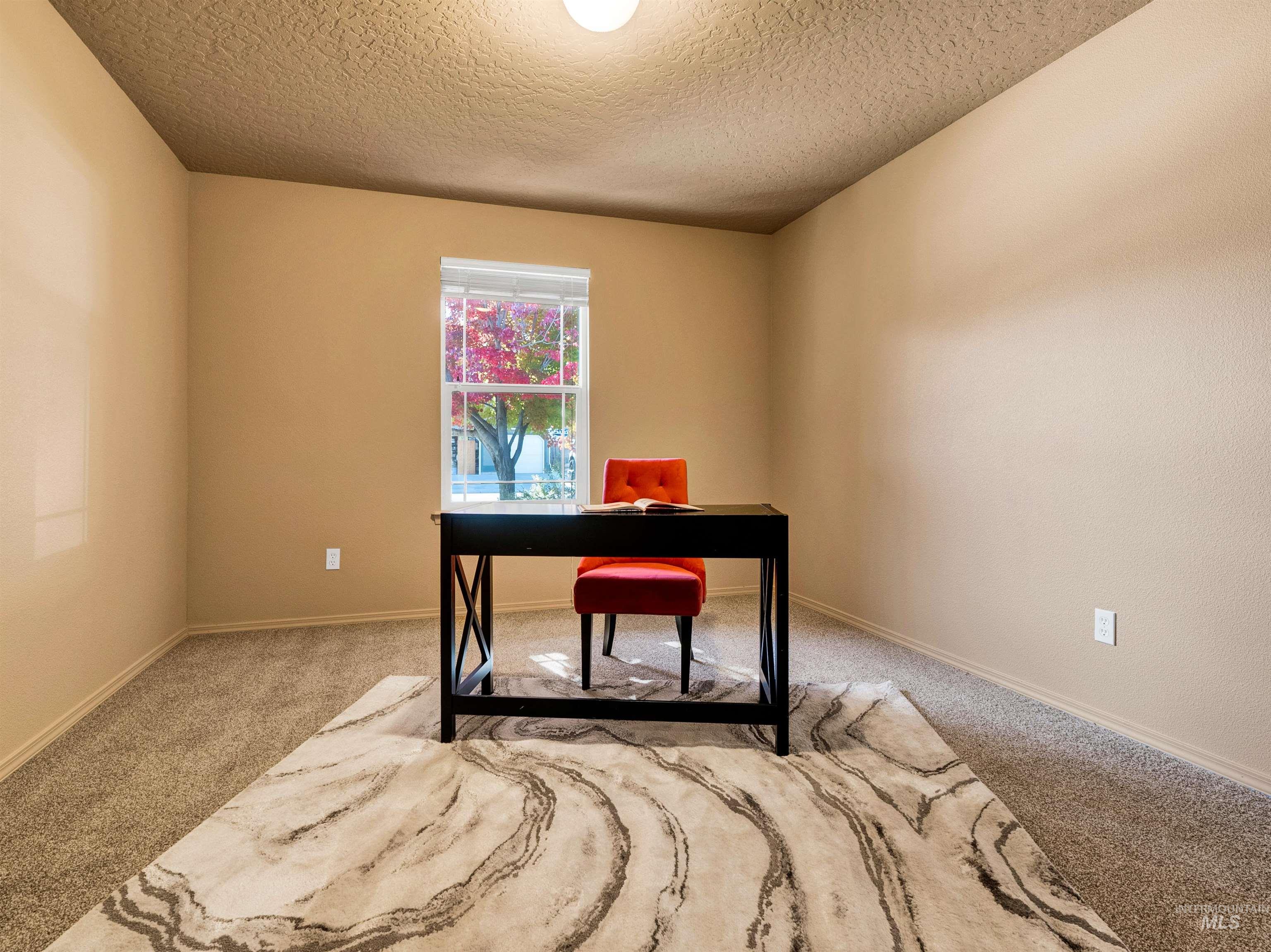 Carpeted office with a textured ceiling and baseboards