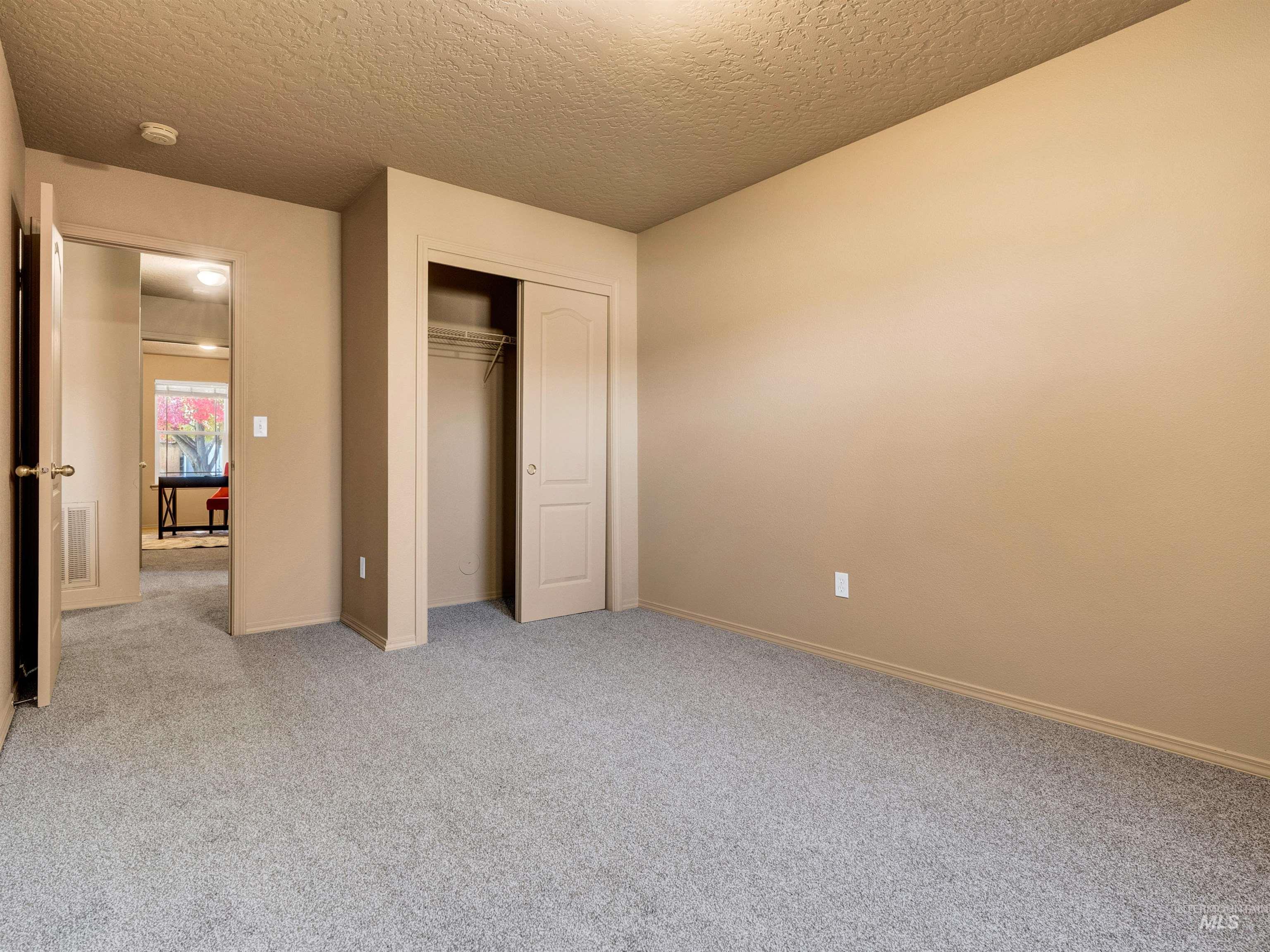Unfurnished bedroom with a textured ceiling, light colored carpet, and a closet
