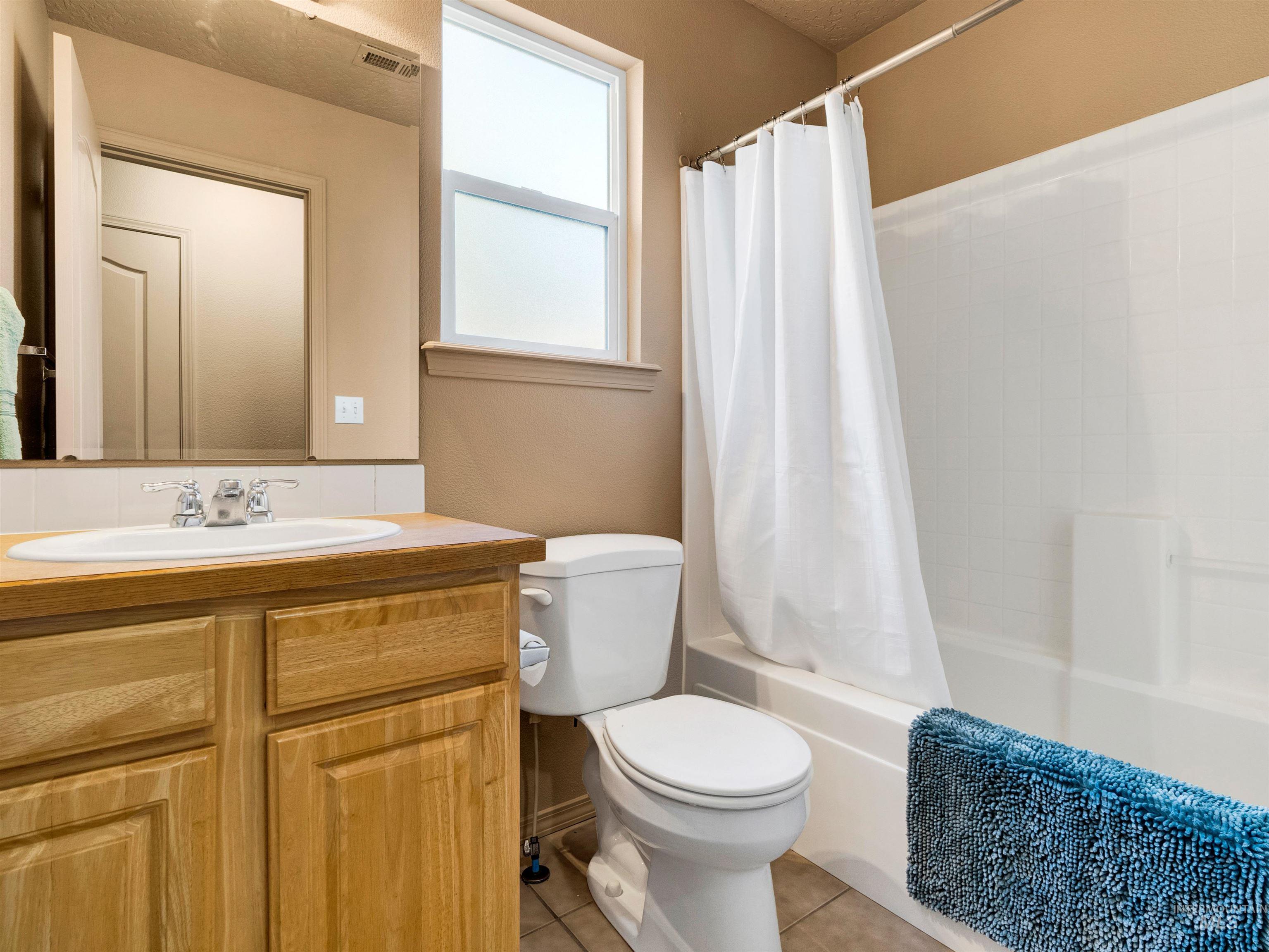 Full bathroom with vanity, light tile patterned floors, shower / bath combo with shower curtain, and a textured ceiling