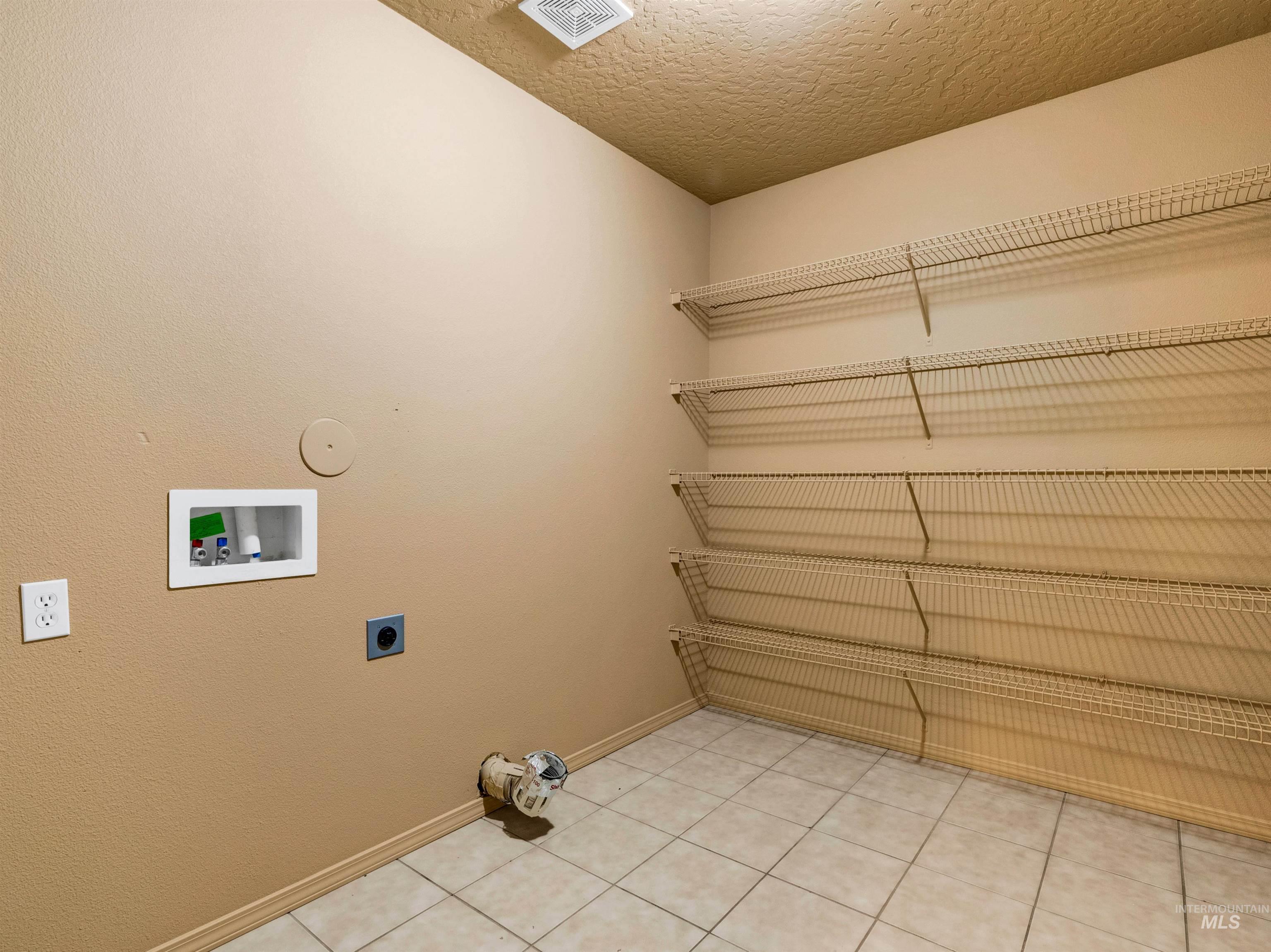 Laundry area with a textured ceiling, hookup for a washing machine, light tile patterned flooring, and hookup for an electric dryer