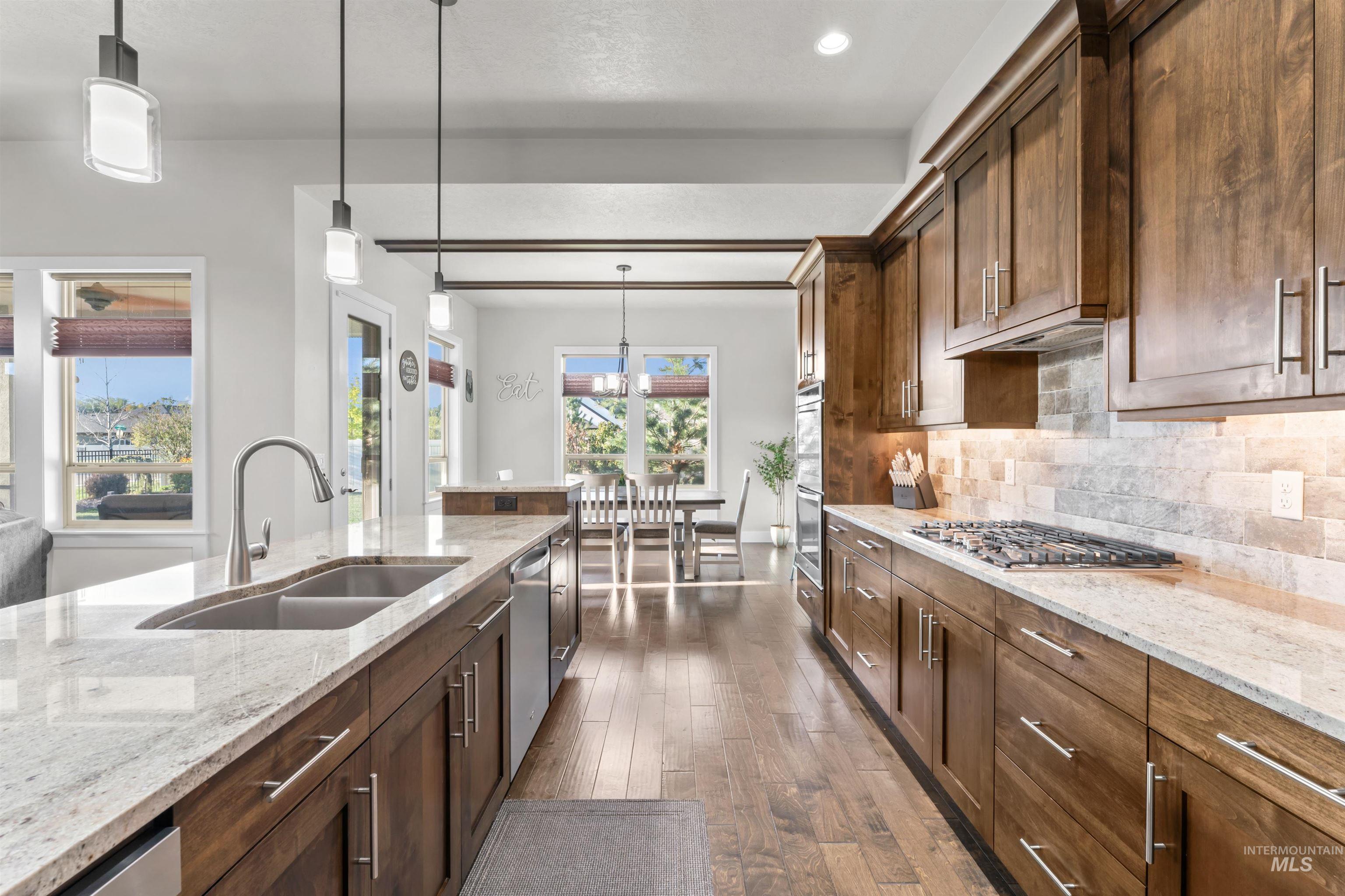 Kitchen featuring hanging light fixtures, light stone counters, tasteful backsplash, dark wood-type flooring, and appliances with stainless steel finishes