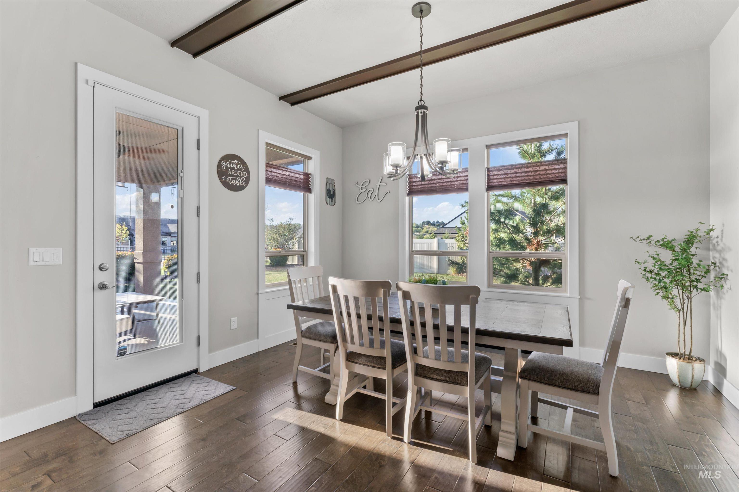 Dining space featuring a chandelier, dark wood-style floors, healthy amount of natural light, and beam ceiling