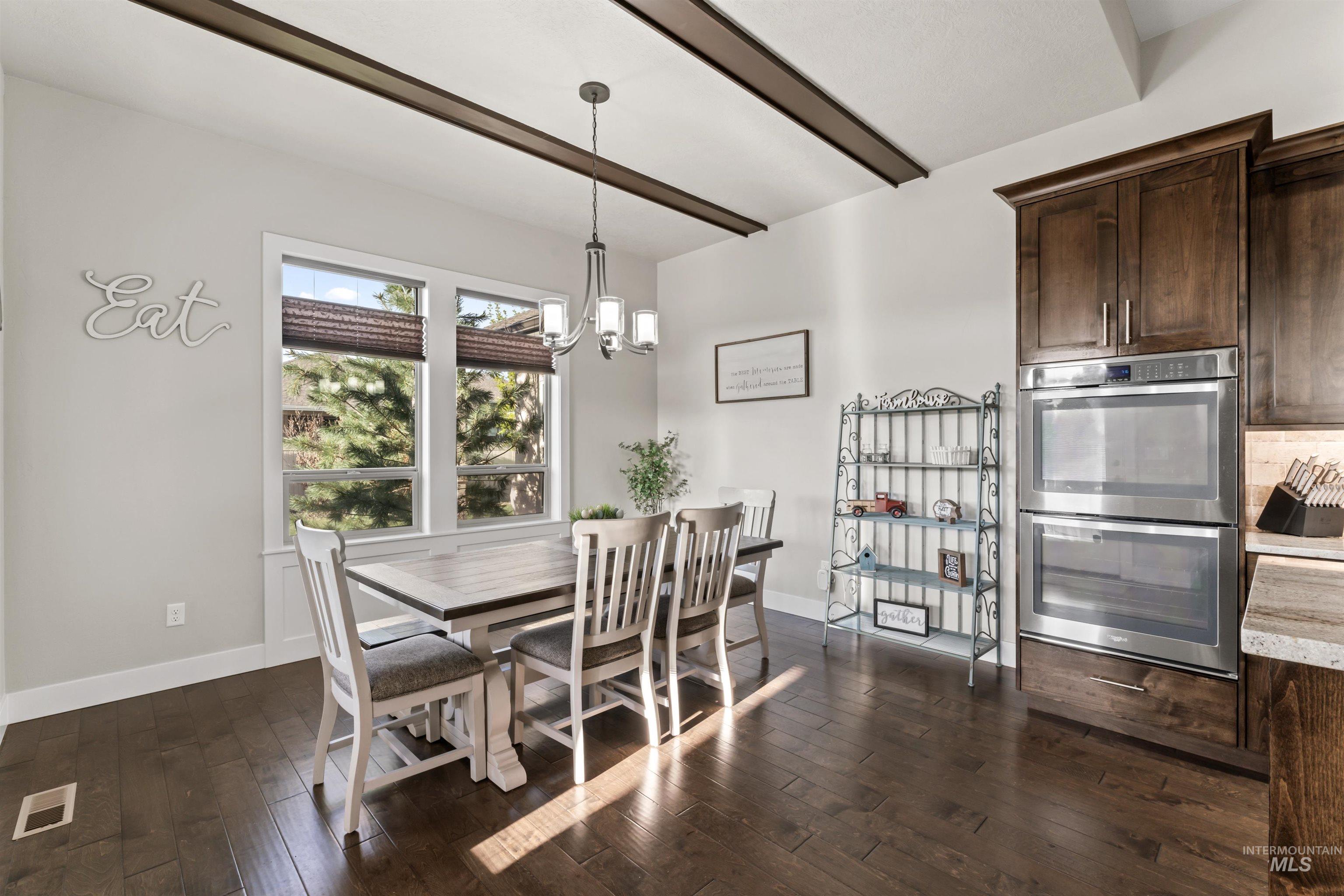 Dining area with dark wood-style floors, a chandelier, and beam ceiling
