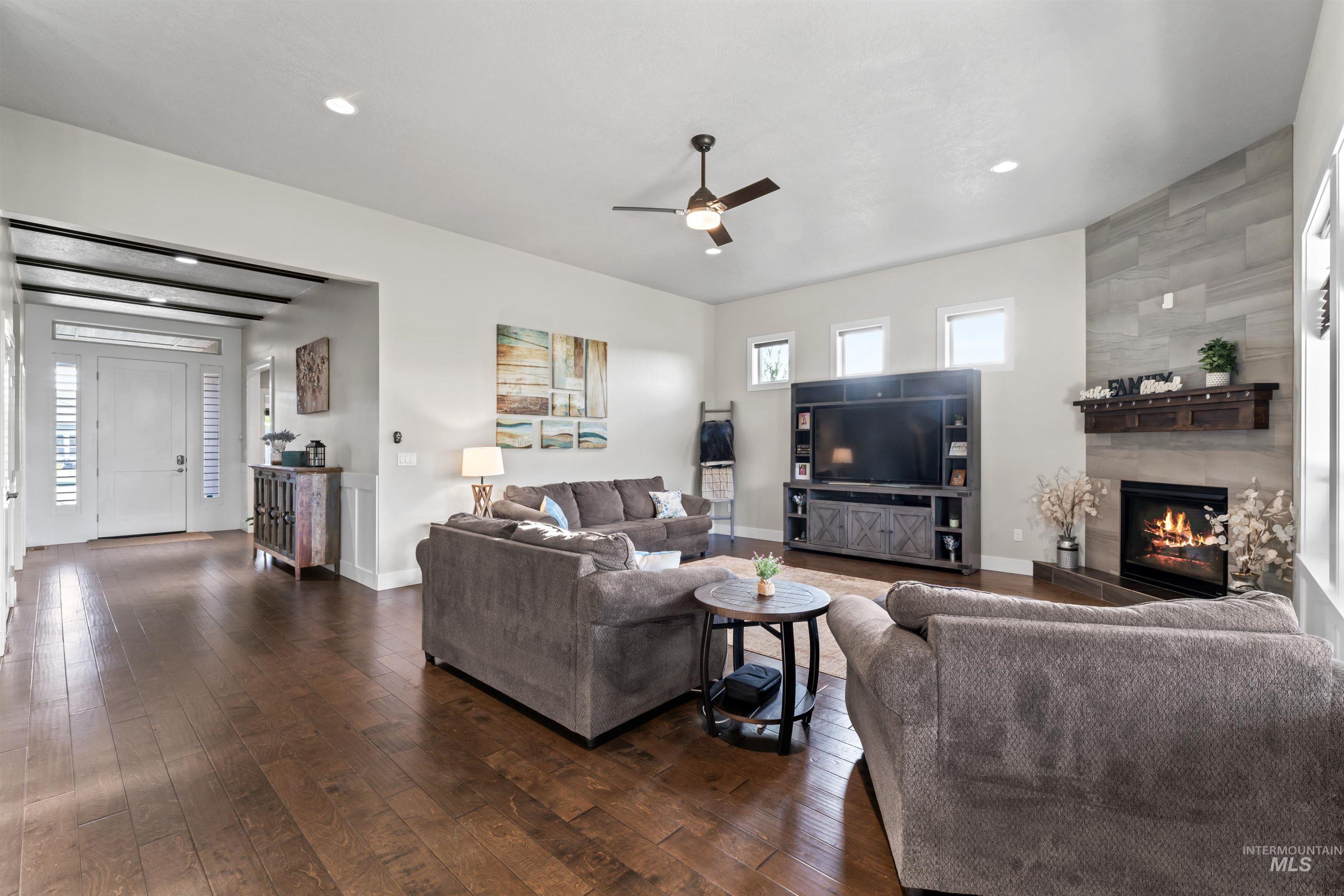 Living room featuring dark wood-style flooring, ceiling fan, a fireplace, and recessed lighting