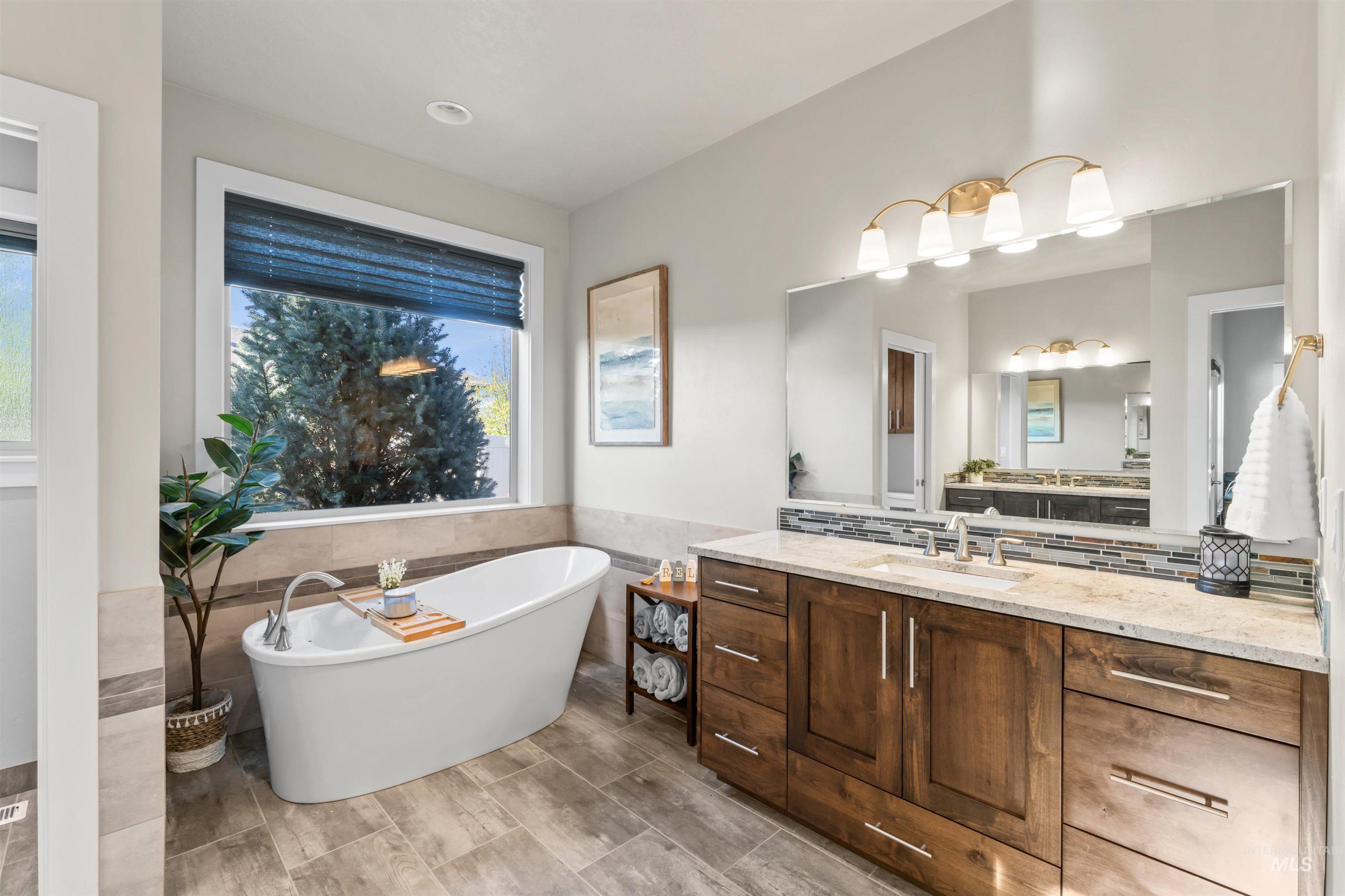 Full bath featuring tile walls, a freestanding tub, vanity, wainscoting, and tasteful backsplash