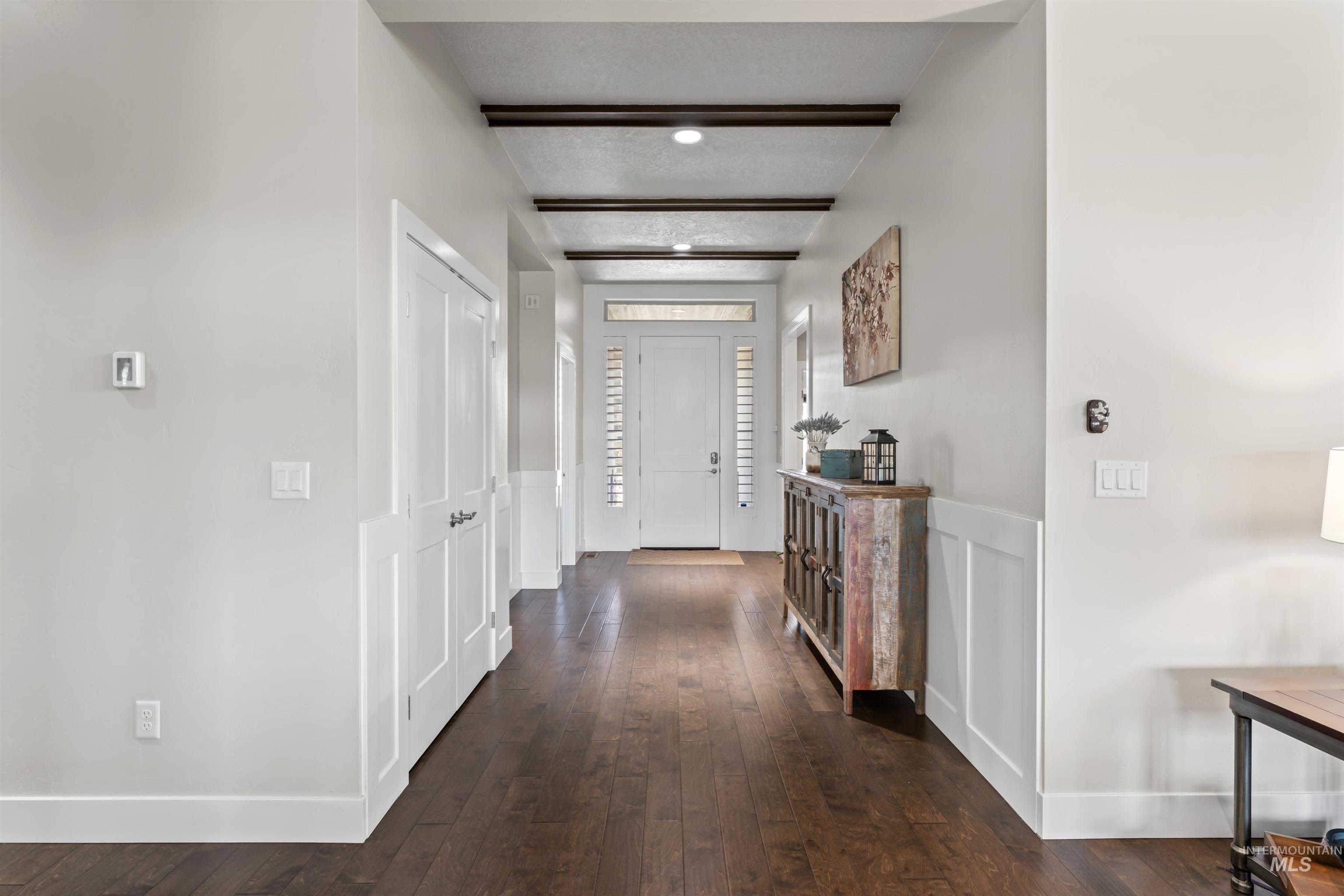 Hall with dark wood-style floors, a decorative wall, wainscoting, and beamed ceiling