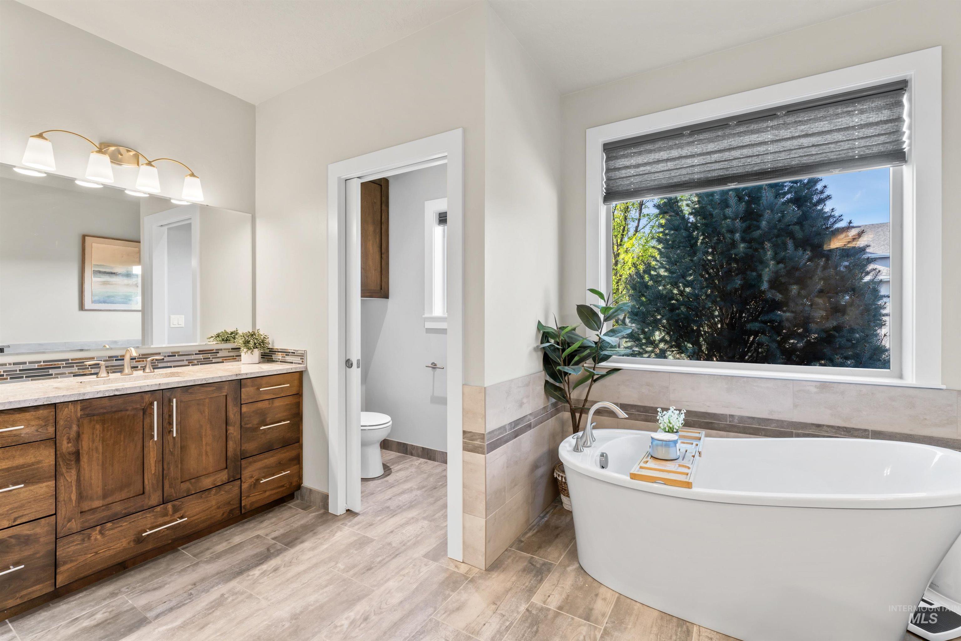Bathroom featuring a freestanding tub, vanity, tile walls, light wood-style flooring, and wainscoting