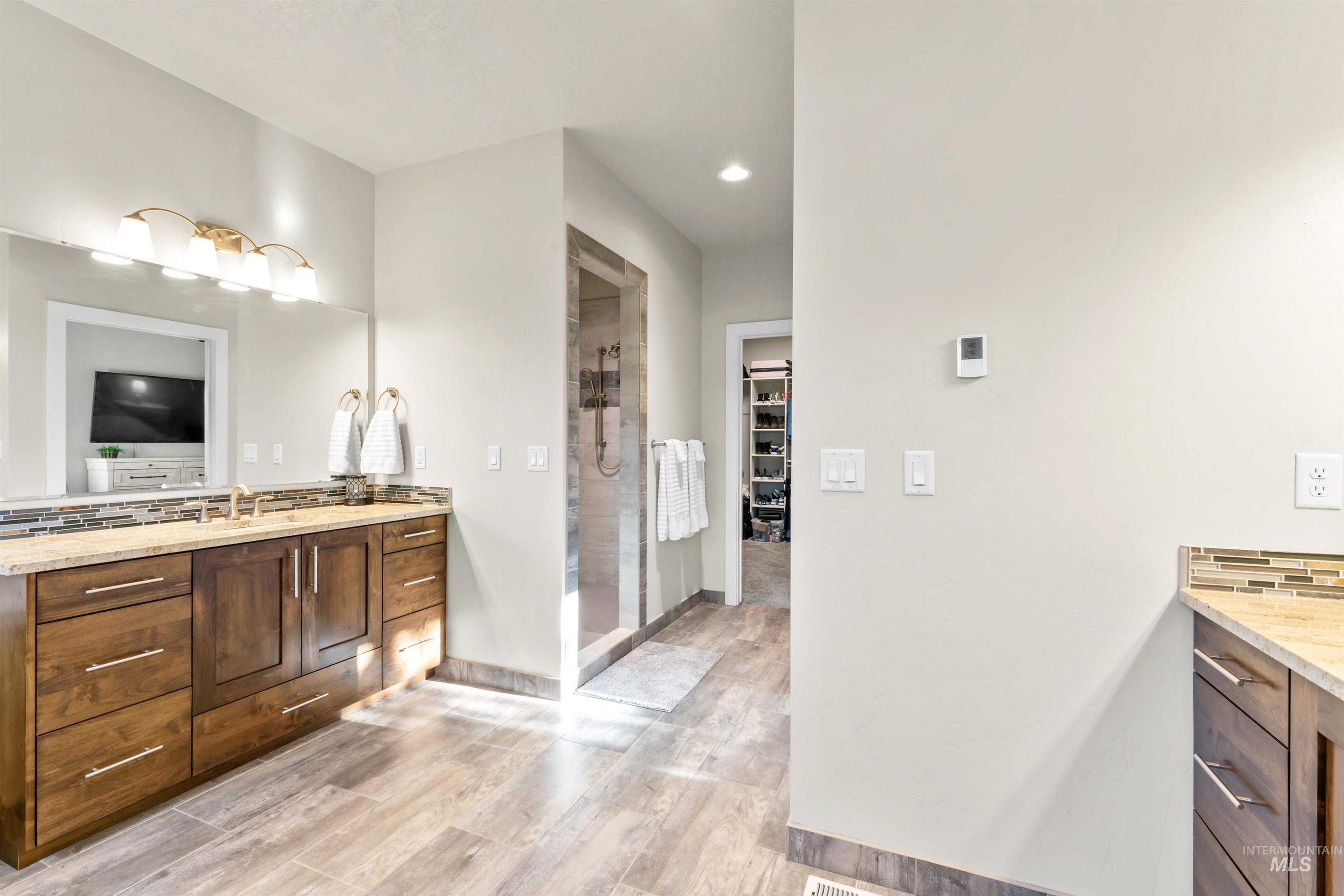 Bathroom featuring vanity, a walk in closet, light wood-style flooring, a stall shower, and recessed lighting