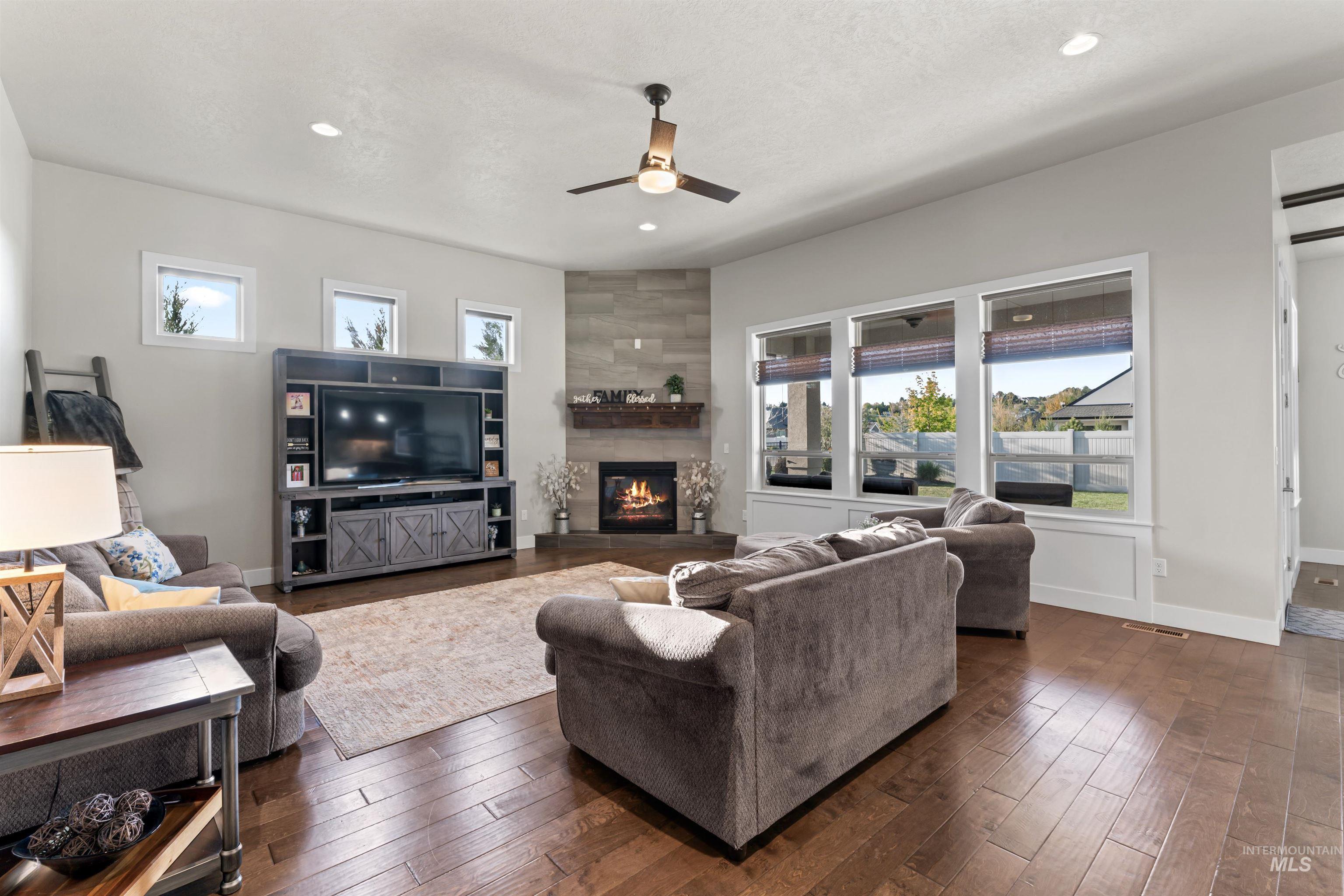 Living room featuring dark wood-style floors, a large fireplace, a ceiling fan, and recessed lighting