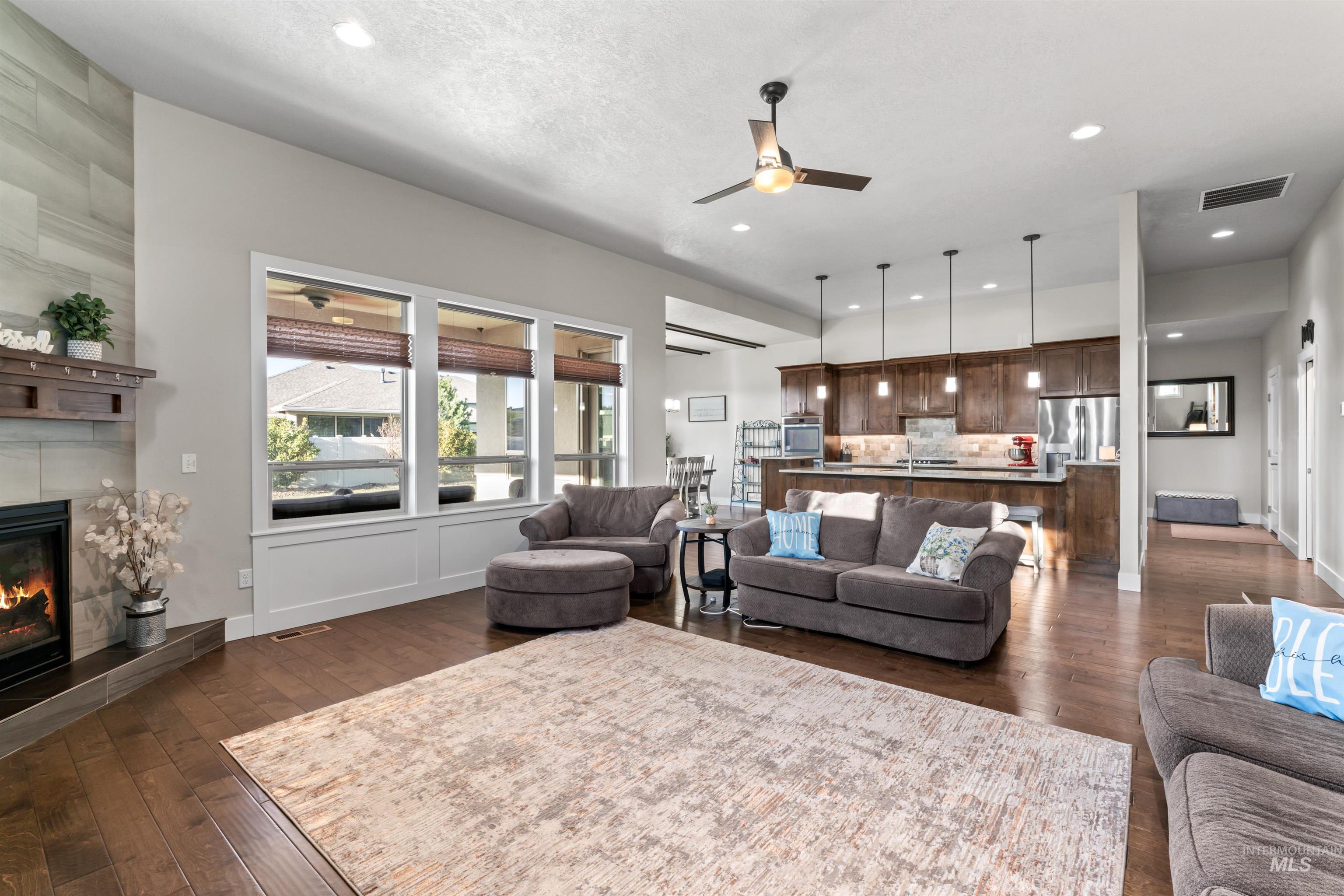 Living room with dark wood-type flooring, a ceiling fan, a fireplace, and recessed lighting