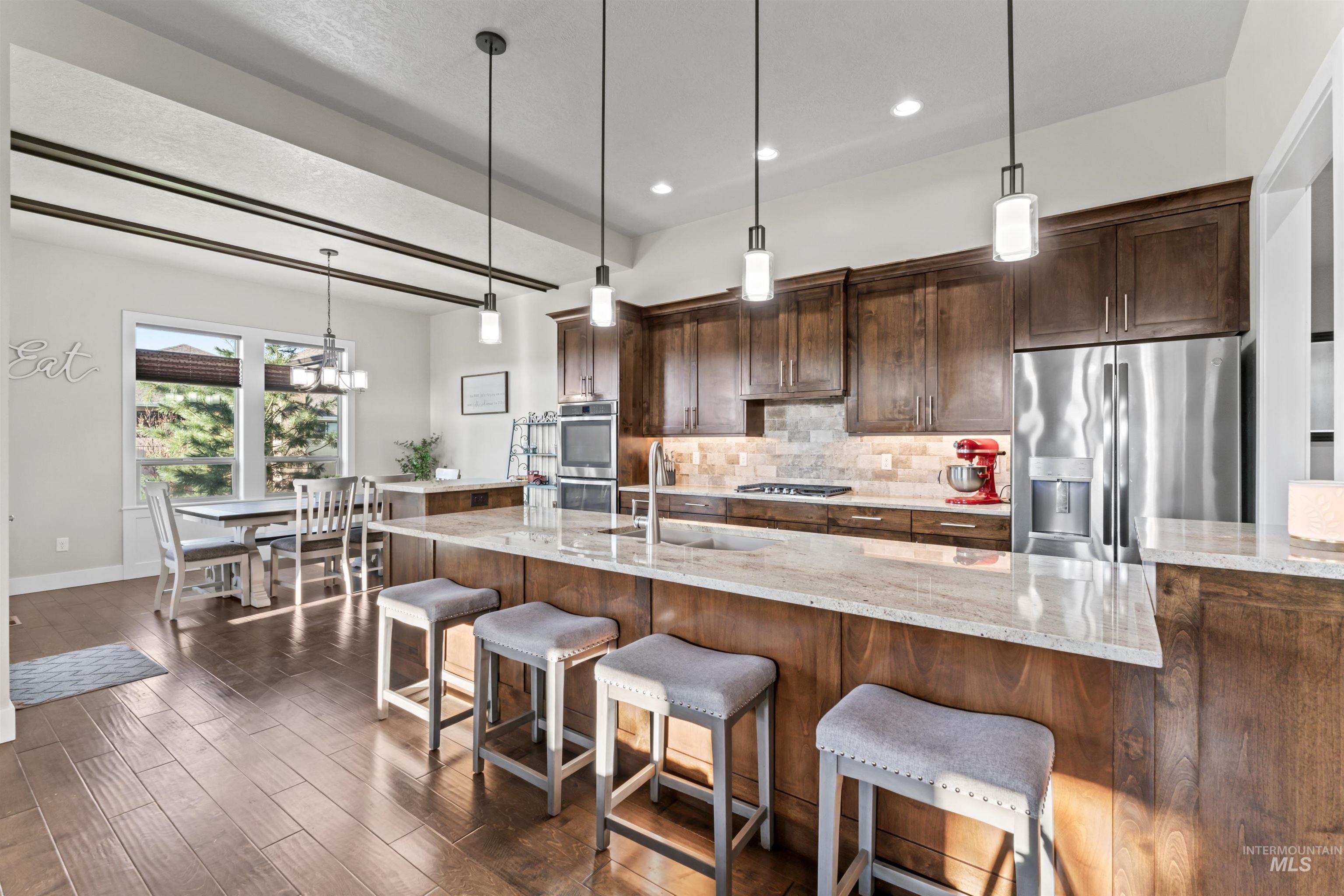 Kitchen featuring decorative backsplash, hanging light fixtures, stainless steel appliances, light stone countertops, and recessed lighting