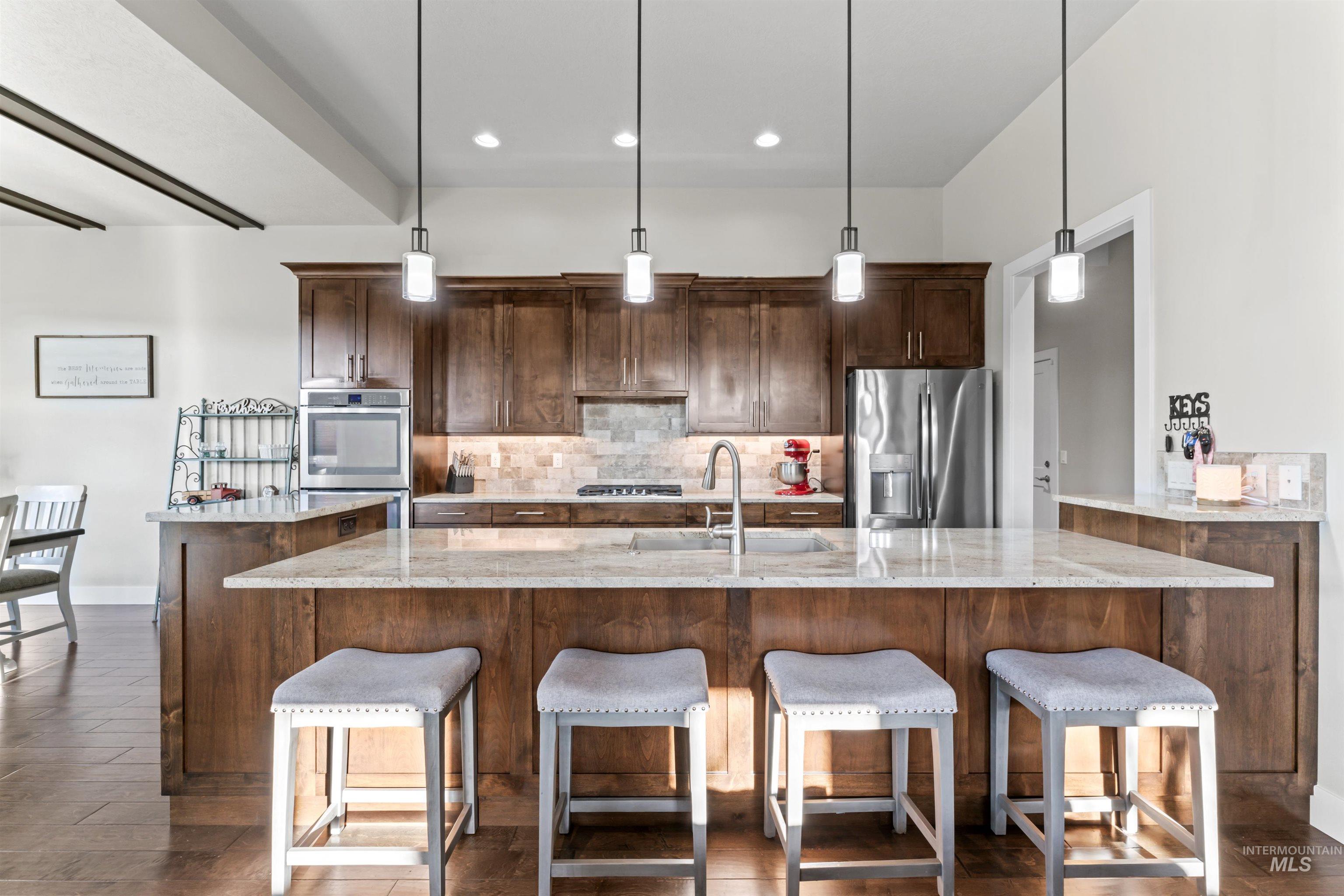 Kitchen featuring backsplash, hanging light fixtures, light stone counters, a kitchen breakfast bar, and stainless steel appliances