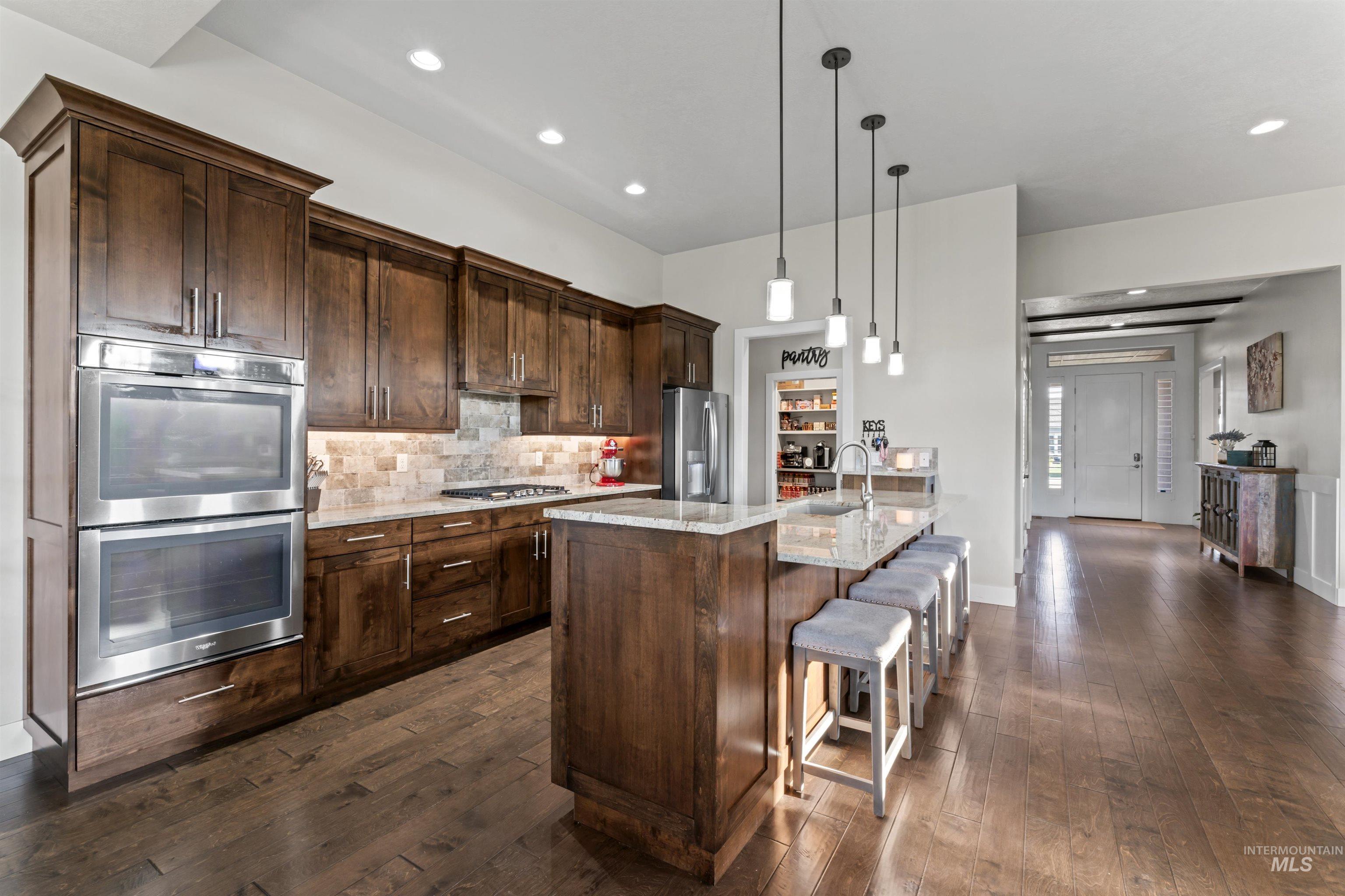 Kitchen with light stone countertops, stainless steel appliances, hanging light fixtures, a breakfast bar, and tasteful backsplash