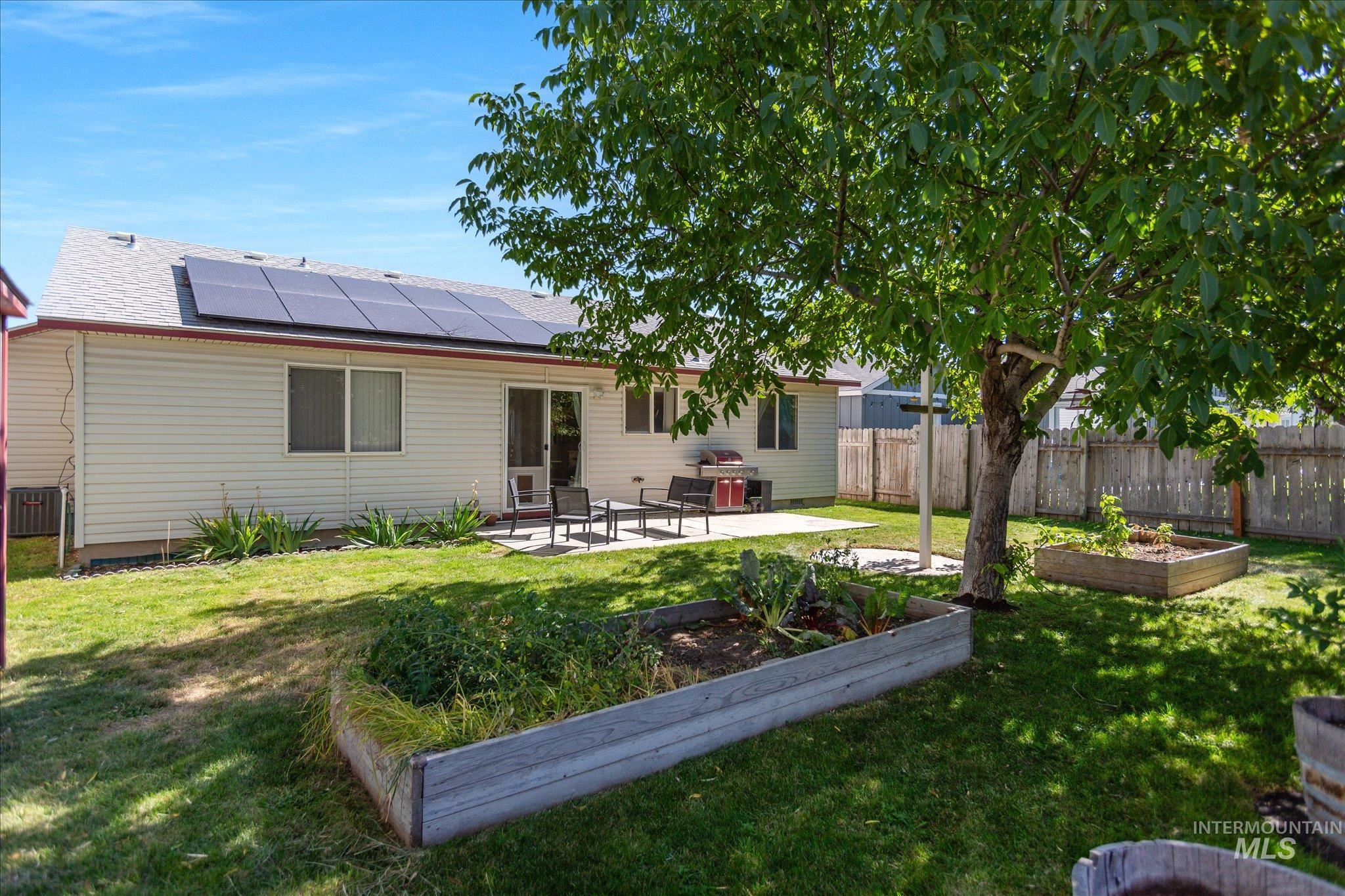 Rear view of property with a garden, a patio, a fenced backyard, and roof mounted solar panels