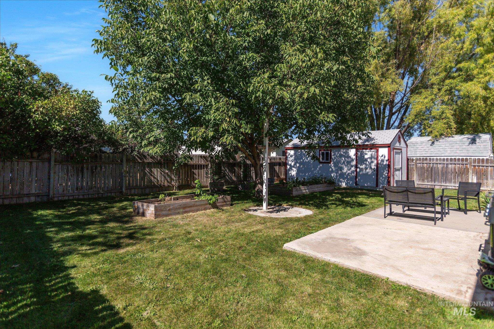 Fenced backyard with a vegetable garden, an outdoor structure, and a patio