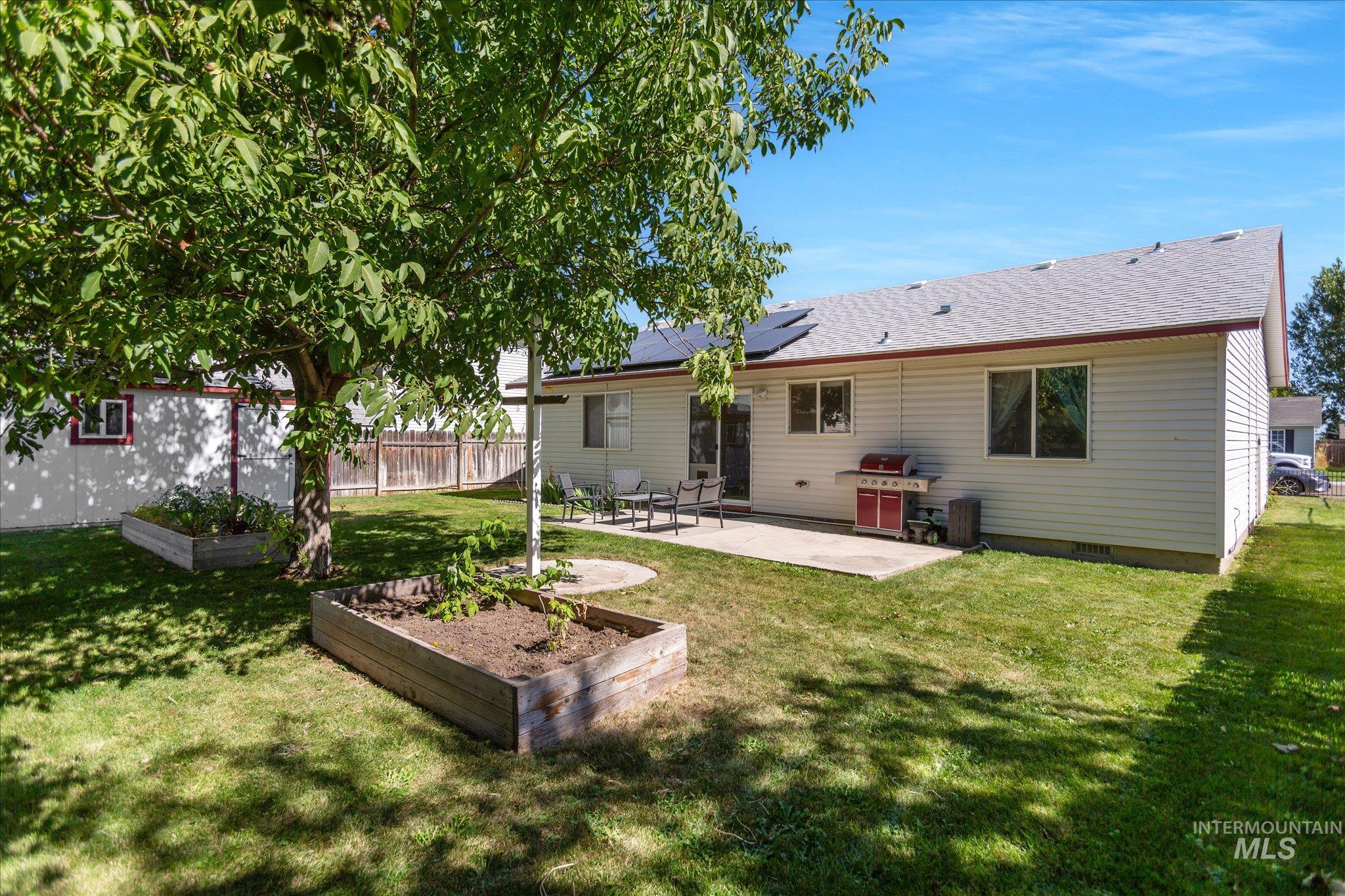 Rear view of property with a vegetable garden, a patio area, roof mounted solar panels, and roof with shingles