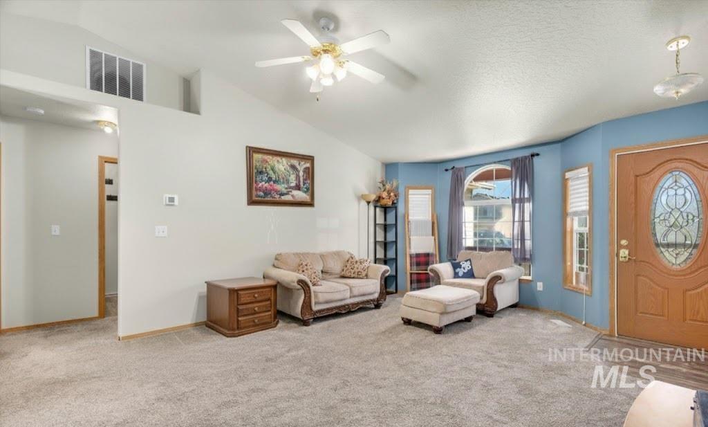 Carpeted living area with vaulted ceiling, a ceiling fan, and a textured ceiling