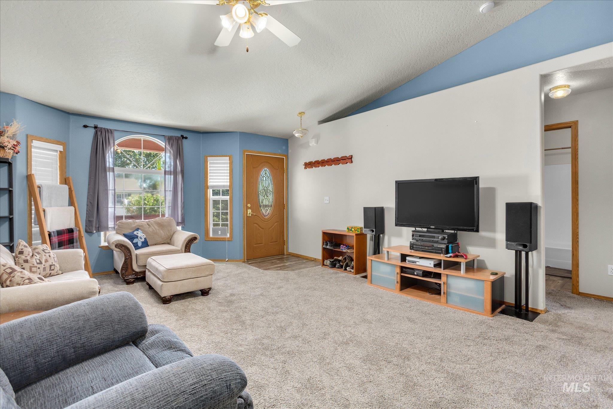 Living area with carpet floors, a ceiling fan, lofted ceiling, and a textured ceiling