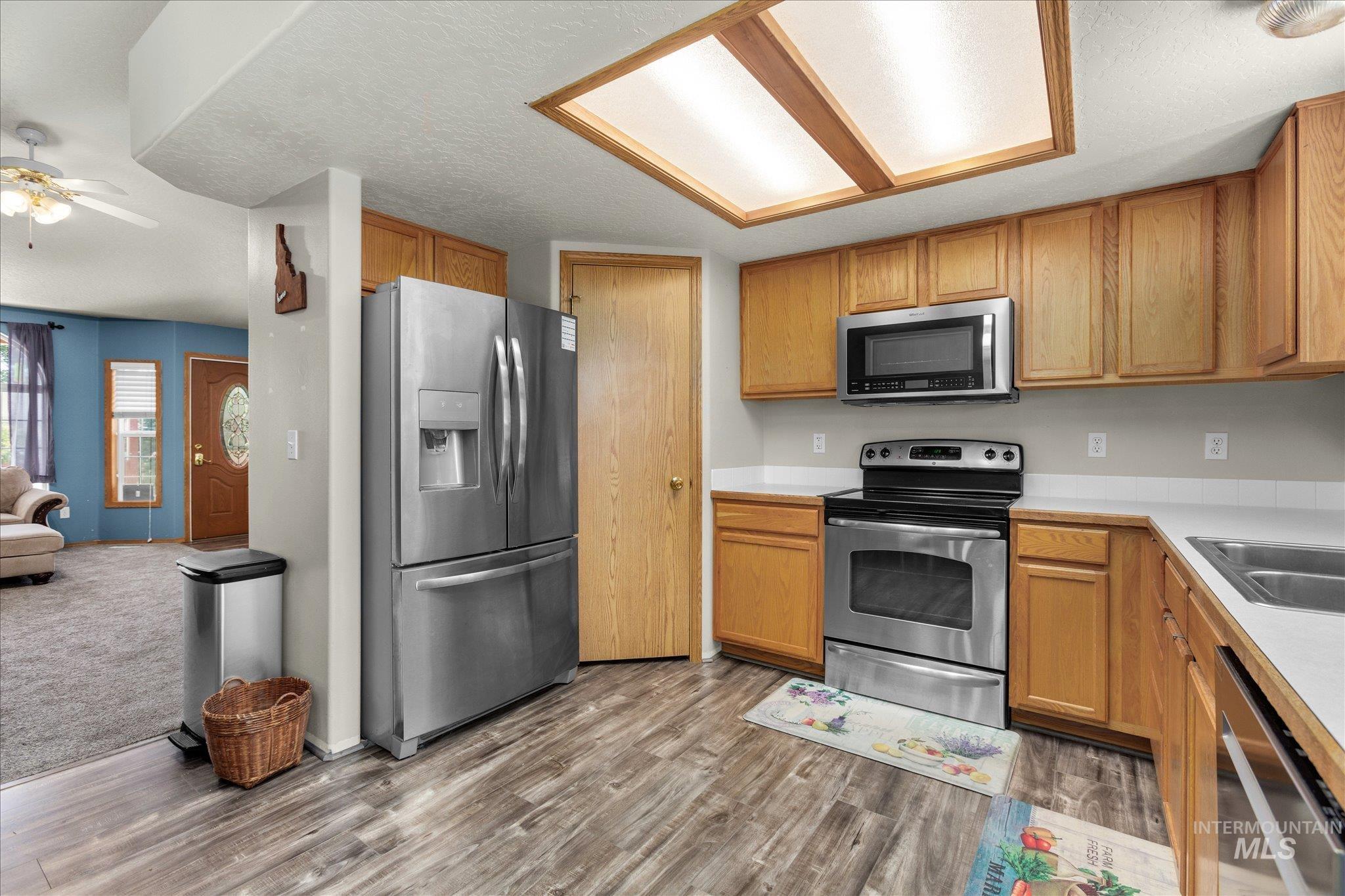 Kitchen featuring stainless steel appliances, light countertops, a textured ceiling, brown cabinets, and dark wood-style flooring