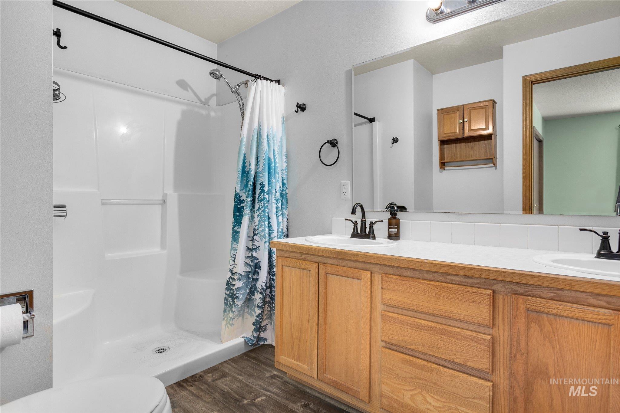 Bathroom featuring a stall shower, double vanity, and dark wood-style floors