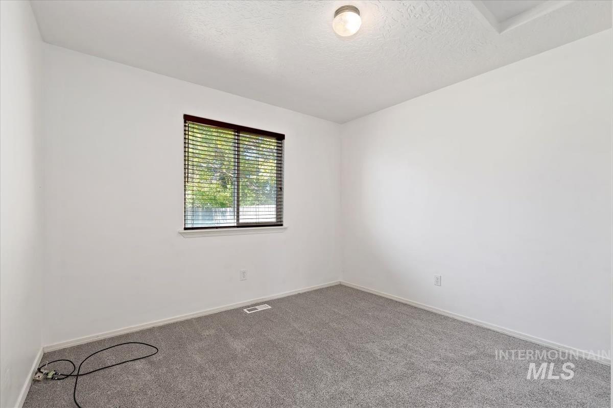 Carpeted empty room with a textured ceiling and baseboards