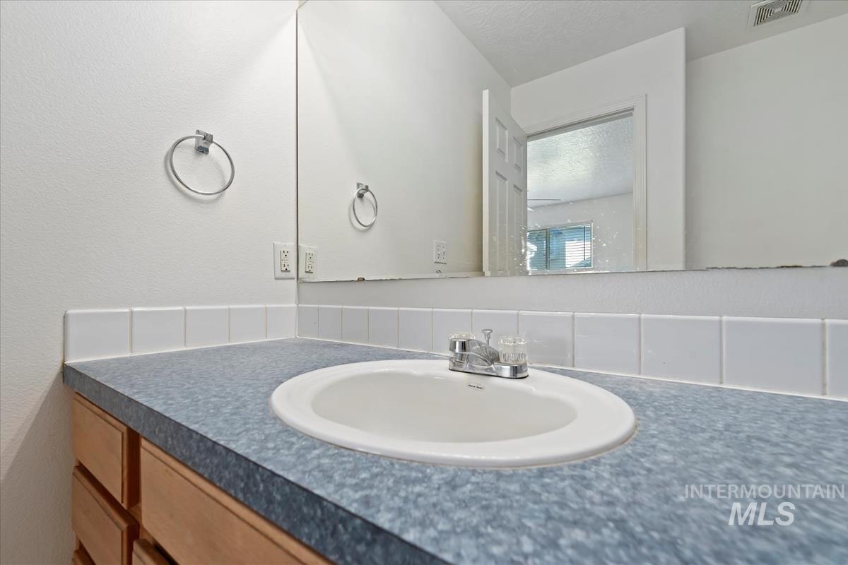 Bathroom with a textured wall, vanity, and tasteful backsplash