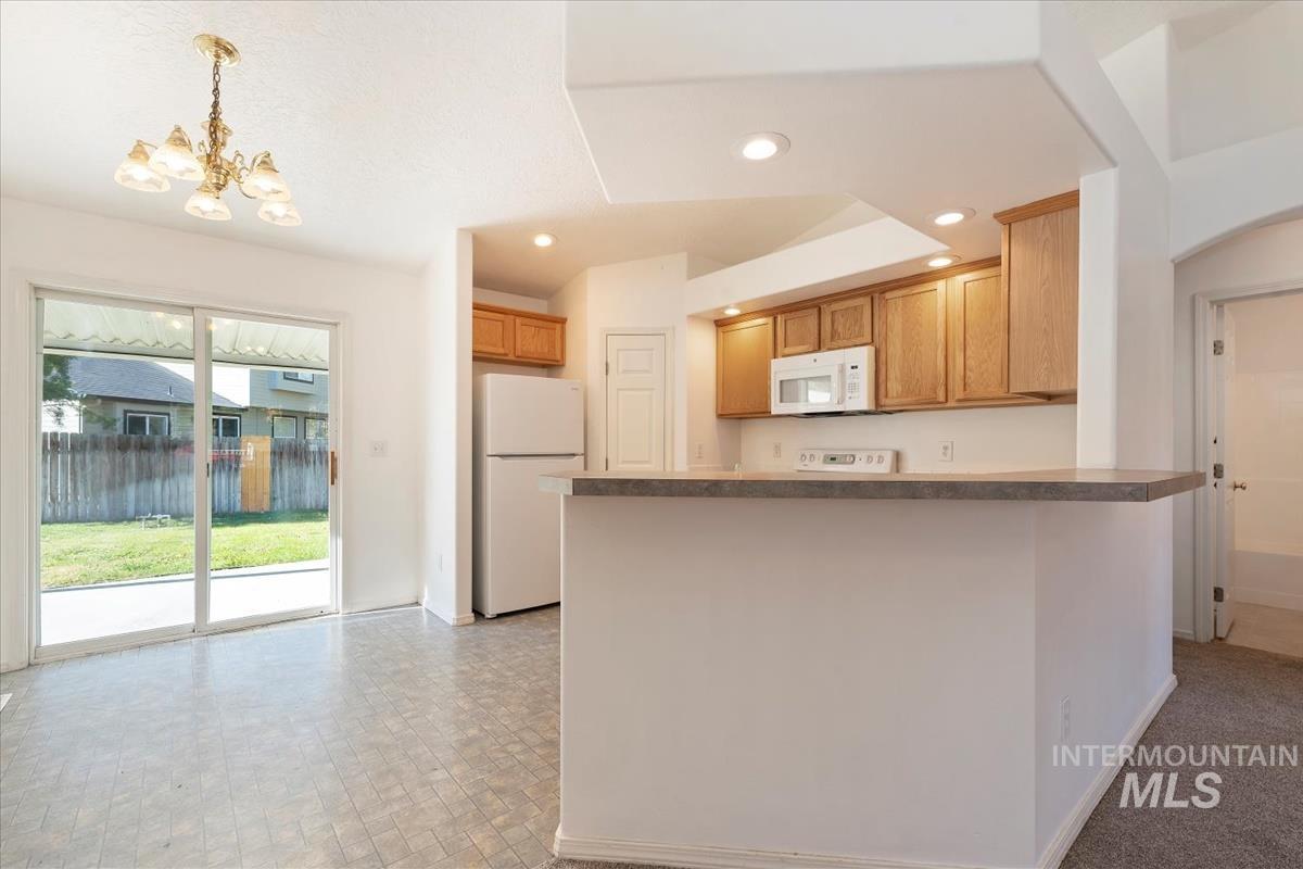 Kitchen with white appliances, a peninsula, recessed lighting, a chandelier, and dark countertops