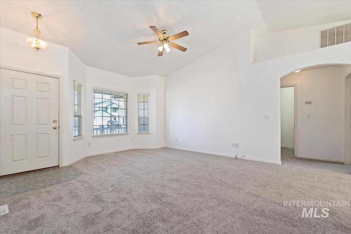 Foyer with light carpet, ceiling fan, arched walkways, and high vaulted ceiling