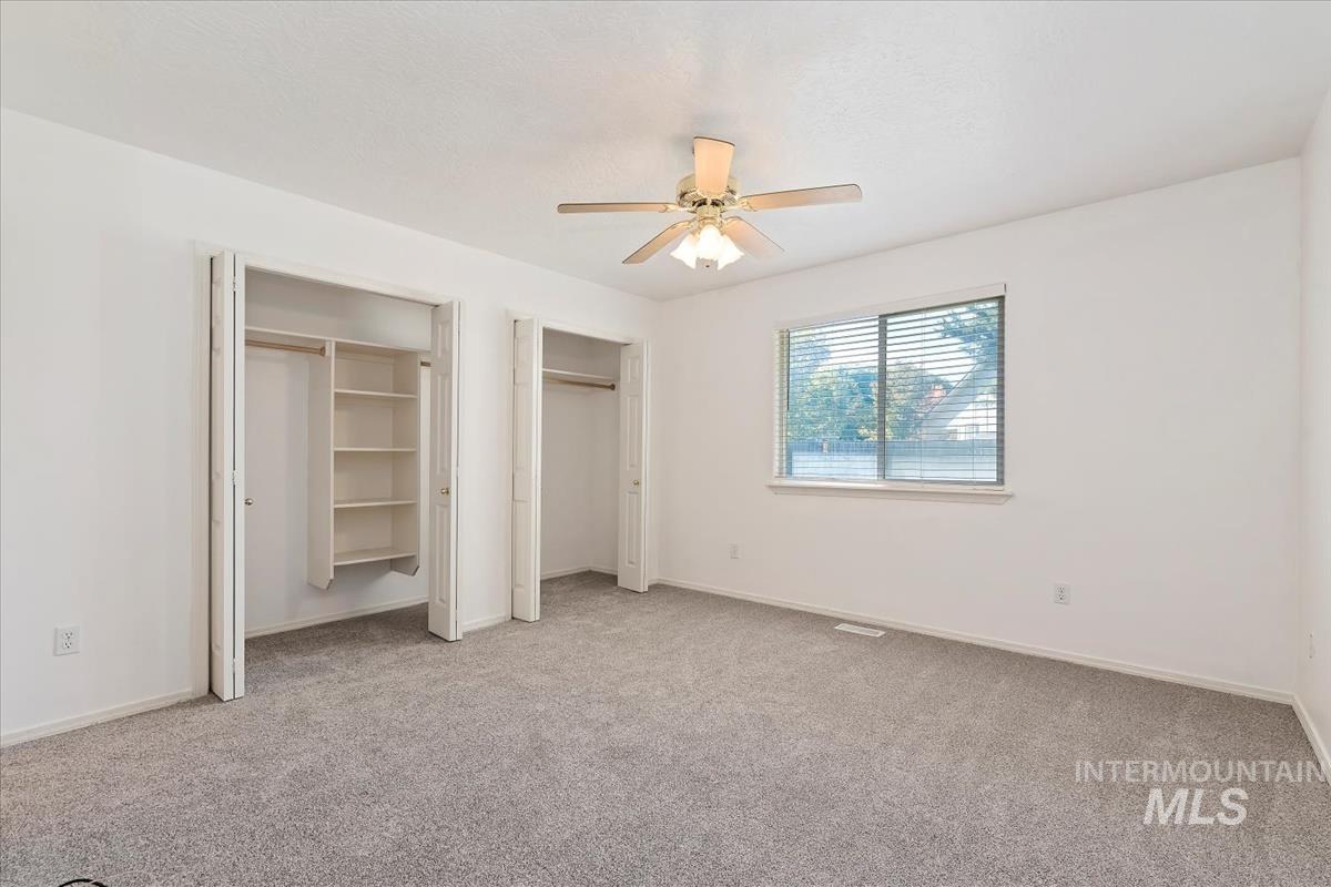 Unfurnished bedroom with multiple closets, light colored carpet, and ceiling fan