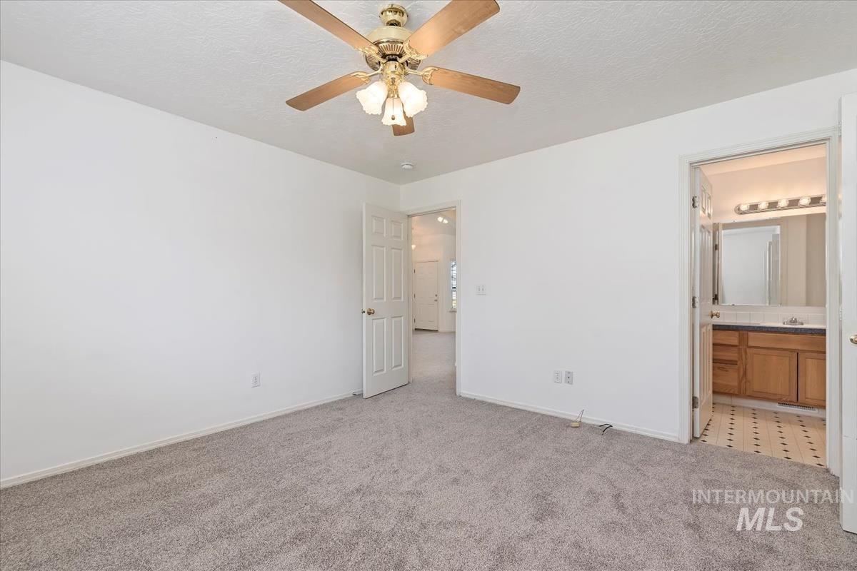 Unfurnished bedroom with light carpet, a textured ceiling, ceiling fan, and ensuite bathroom