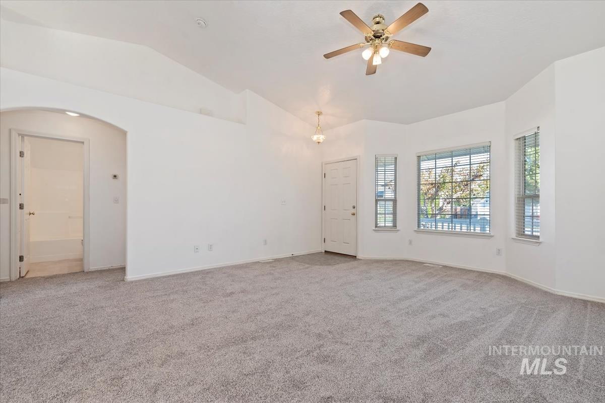 Unfurnished room featuring light carpet, vaulted ceiling, a ceiling fan, and arched walkways